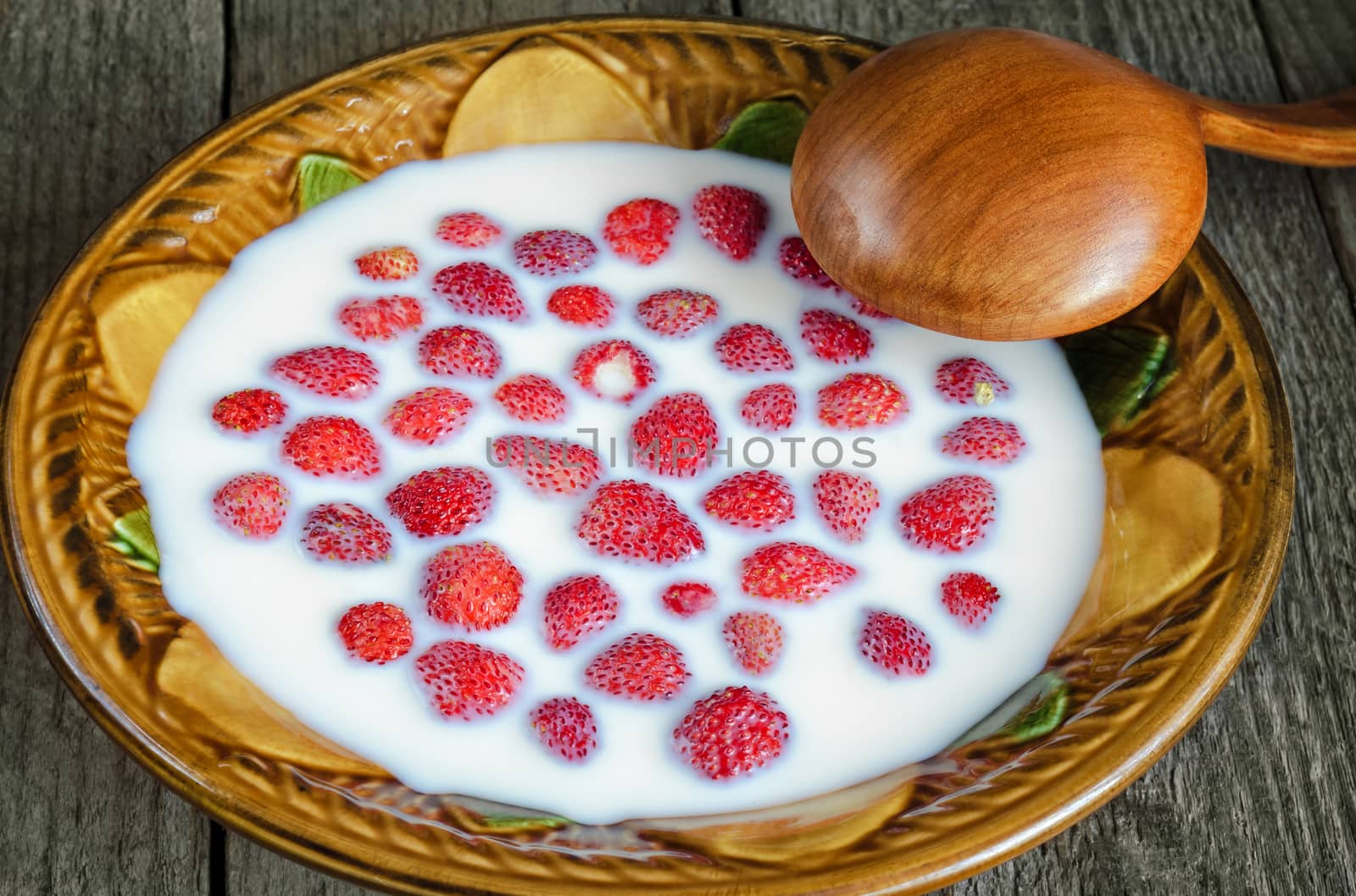 Strawberry with milk in a ceramic bowl and spoon on old wooden background