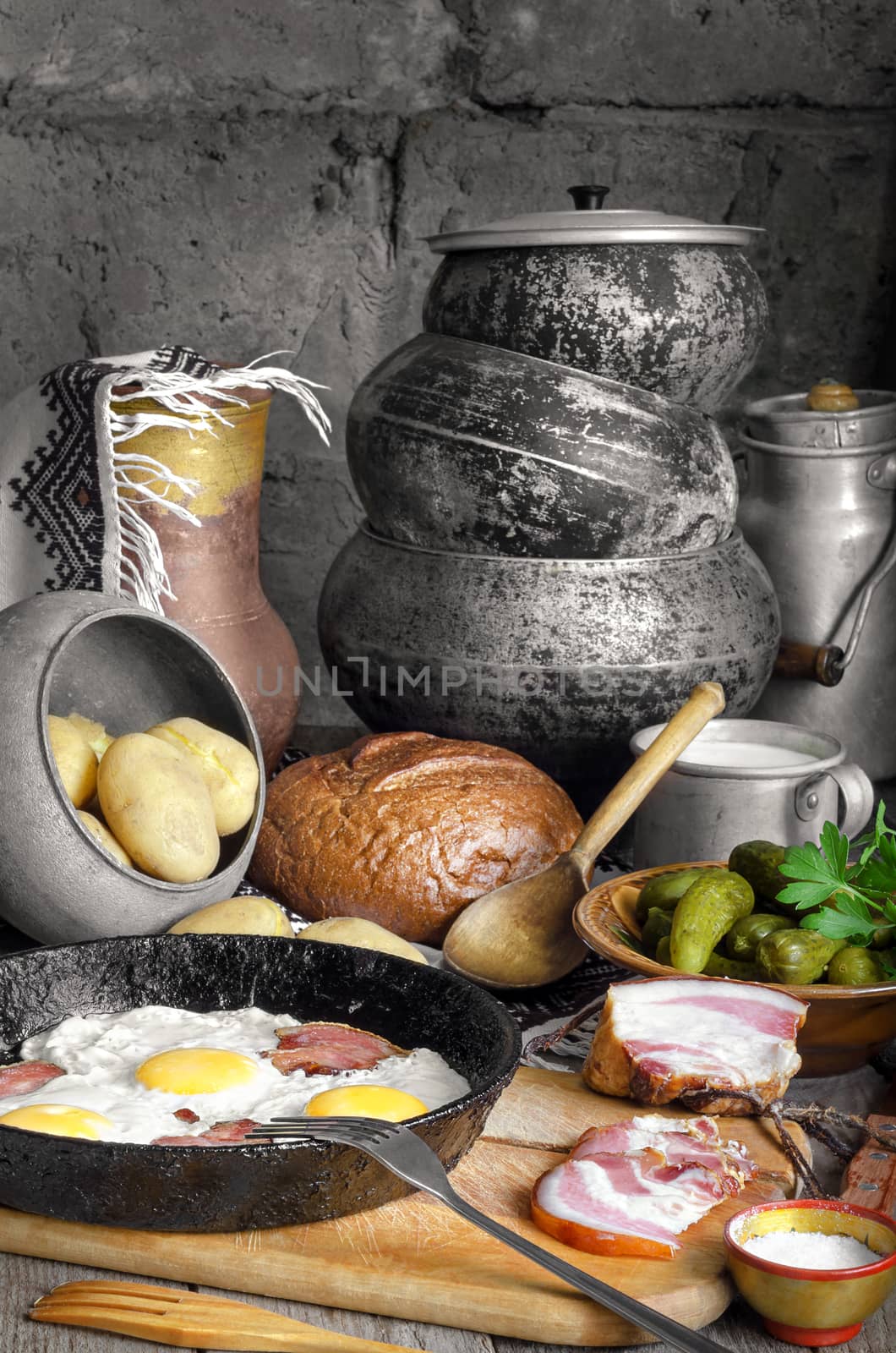 Bacon and eggs, boiled potatoes, pickles. On the background of antique dishes and bread.