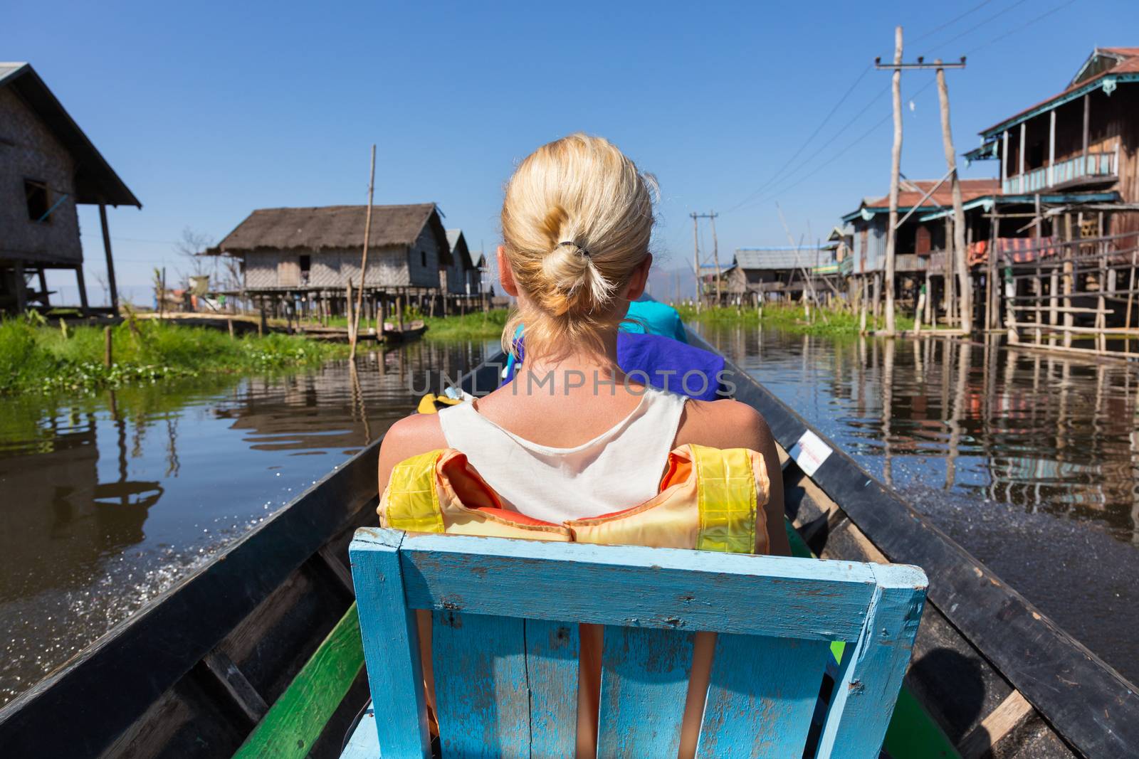 Rear view of female Caucasian tourist traveling by colorful traditional wooden boat on Inle lake, Burma, Myanmar.