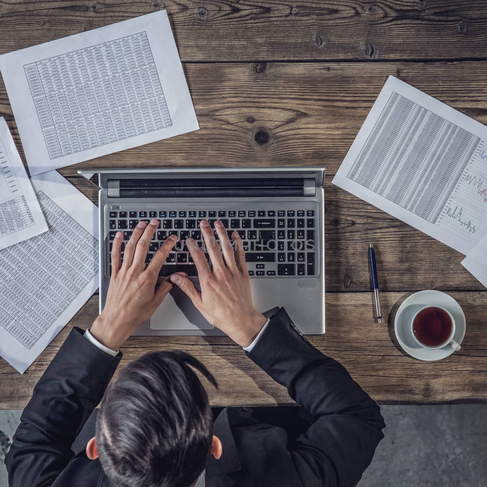 Businessman working on laptop with financial documents, top view