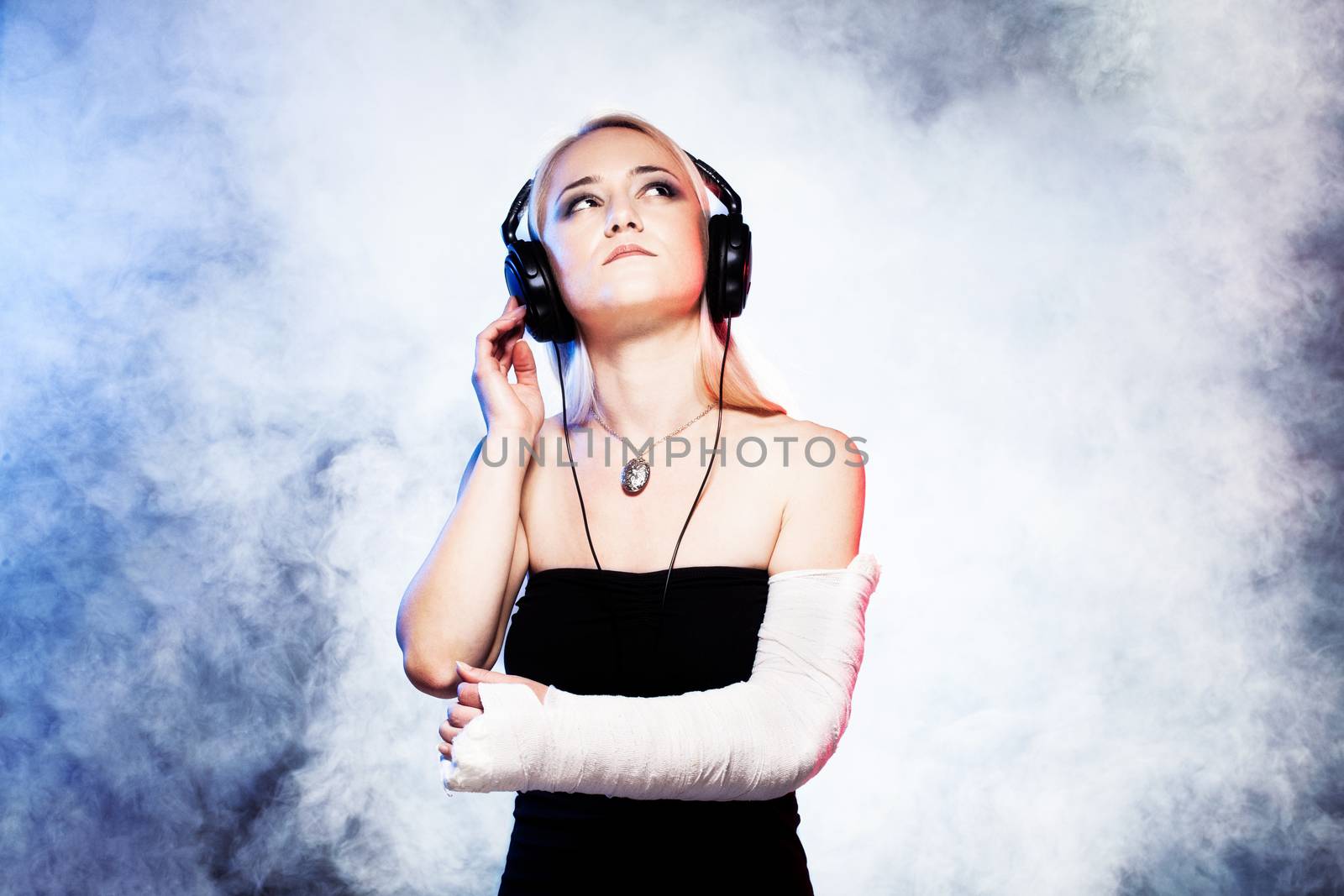 sexy girl with broken arm listening music on headphones and dancing, disco smoke in the background