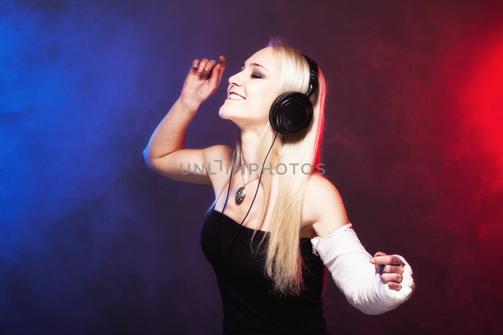 sexy girl with broken arm listening music on headphones and dancing, disco smoke in the background