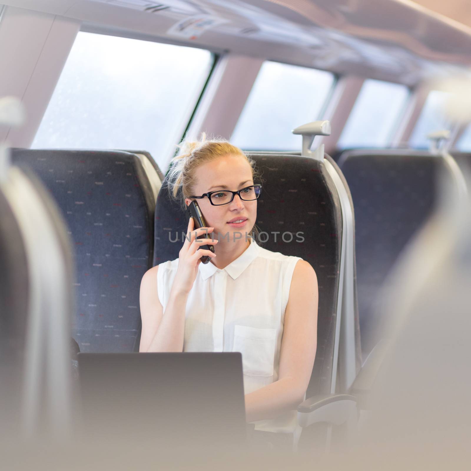 Businesswoman talking on cellphone and working on laptop while traveling by train. Business travel concept.