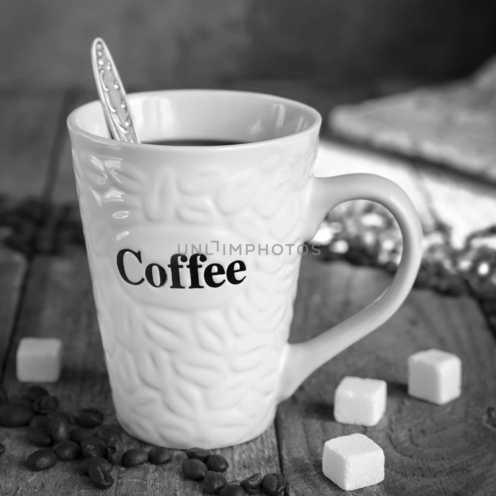 Mug of coffee on the old Board, spilled coffee beans and sugar cubes. Morning light. Black and white
