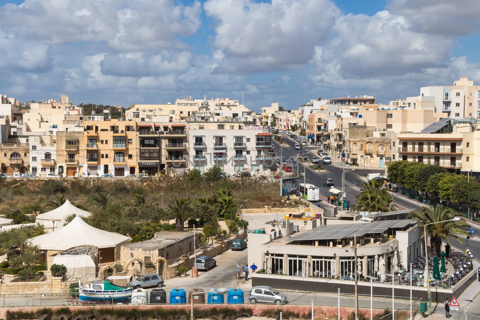 City Marsascala on the island Malta. Residential houses and a road with cars. Many clouds on the blue sky.