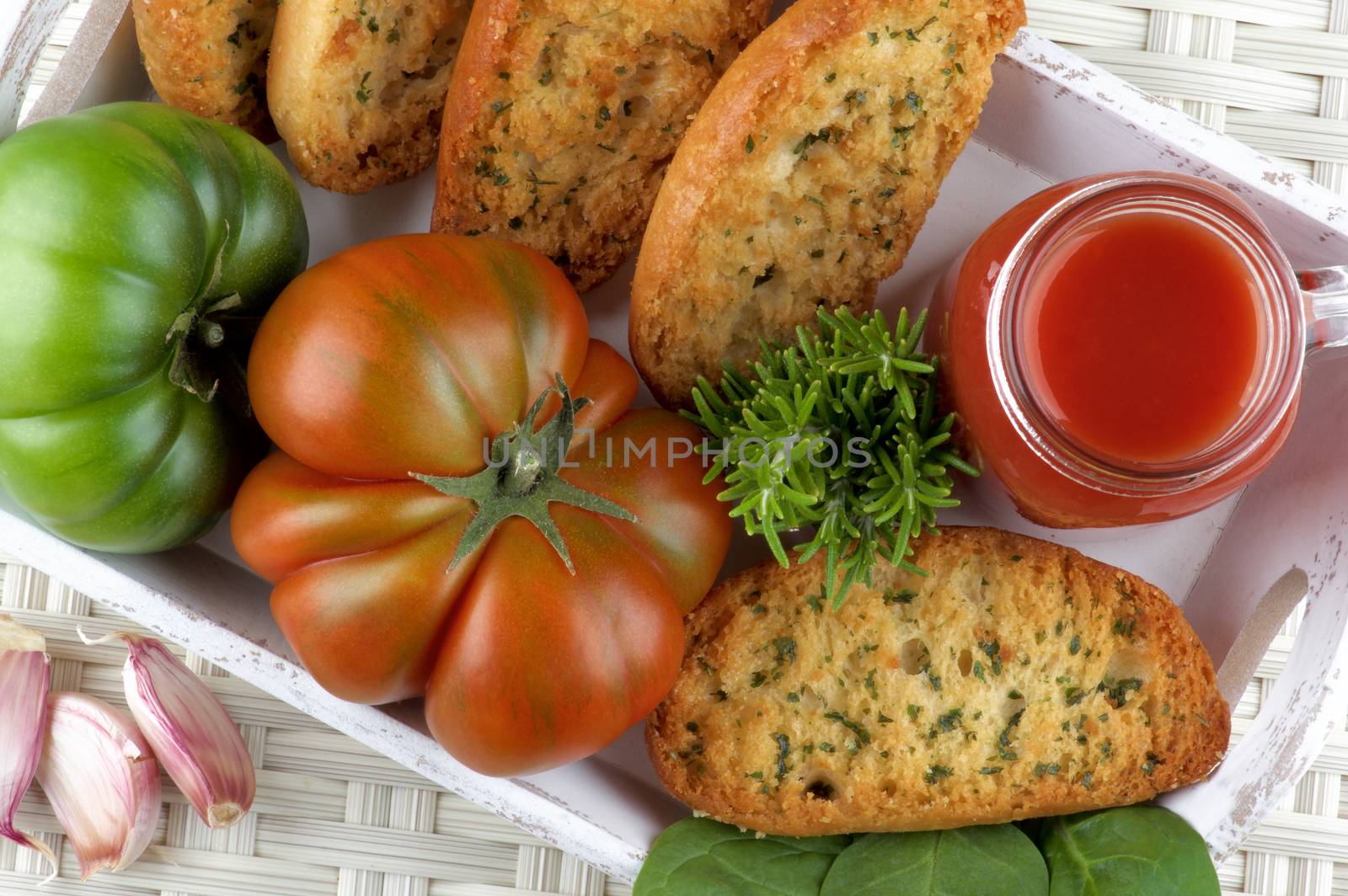 Tomato Juice in Glass Jar with Raw Tomatoes, Crispy Bread and Fresh Herbs closeup into White Wooden Tray. Top View on Wicker background
