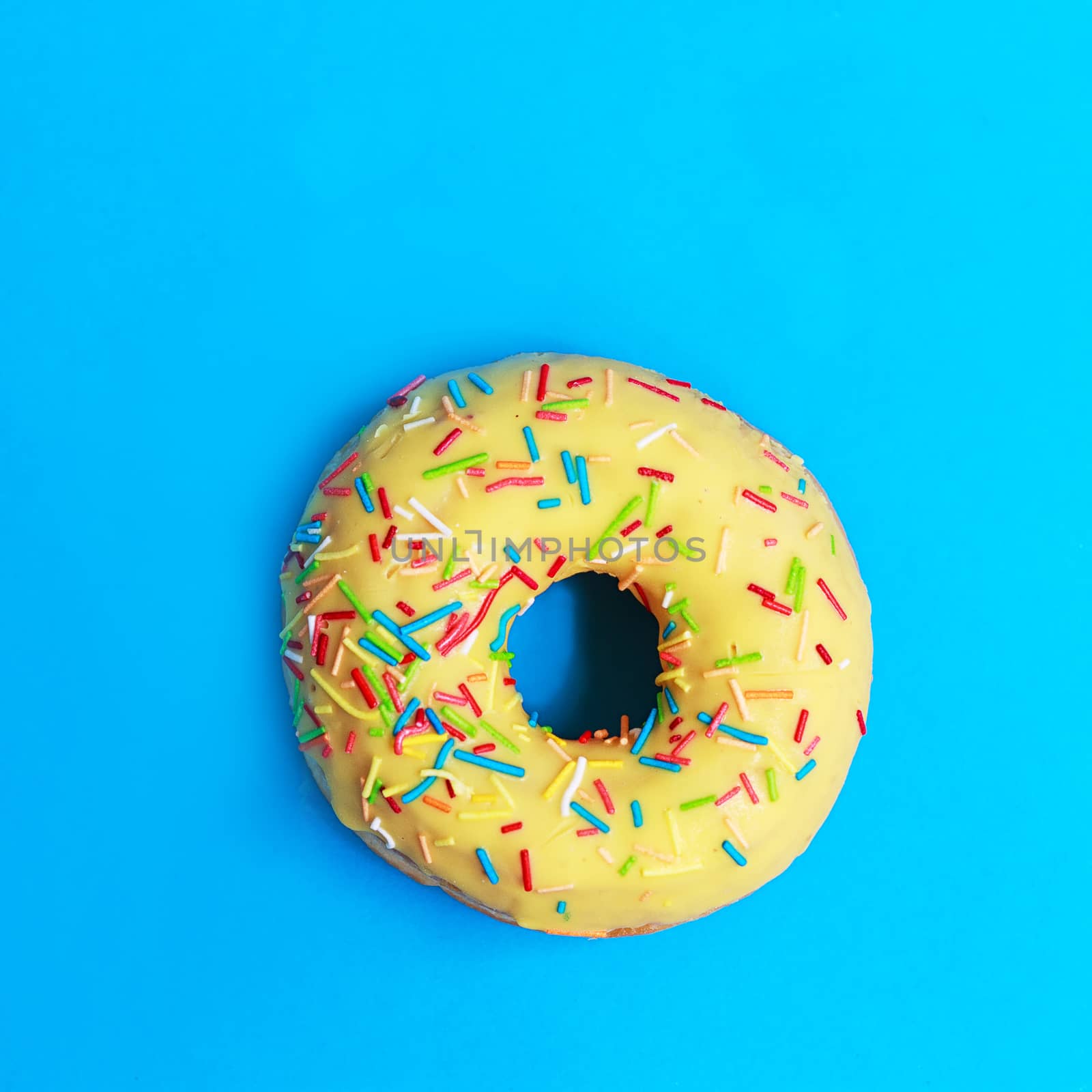 Bright yellow round Donuts with colorful sprinkles on a blue background