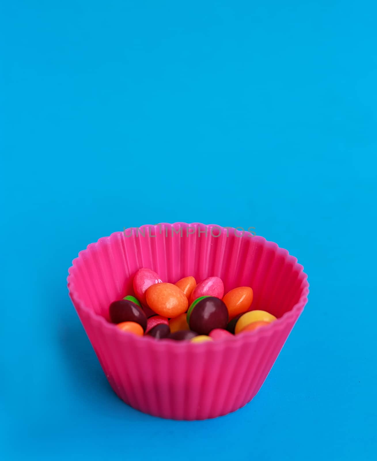 Colorful candies in cupcake case on the blue background