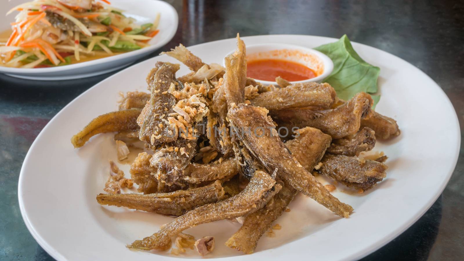 Fried fish topped with garlic served on dish with chili sauce