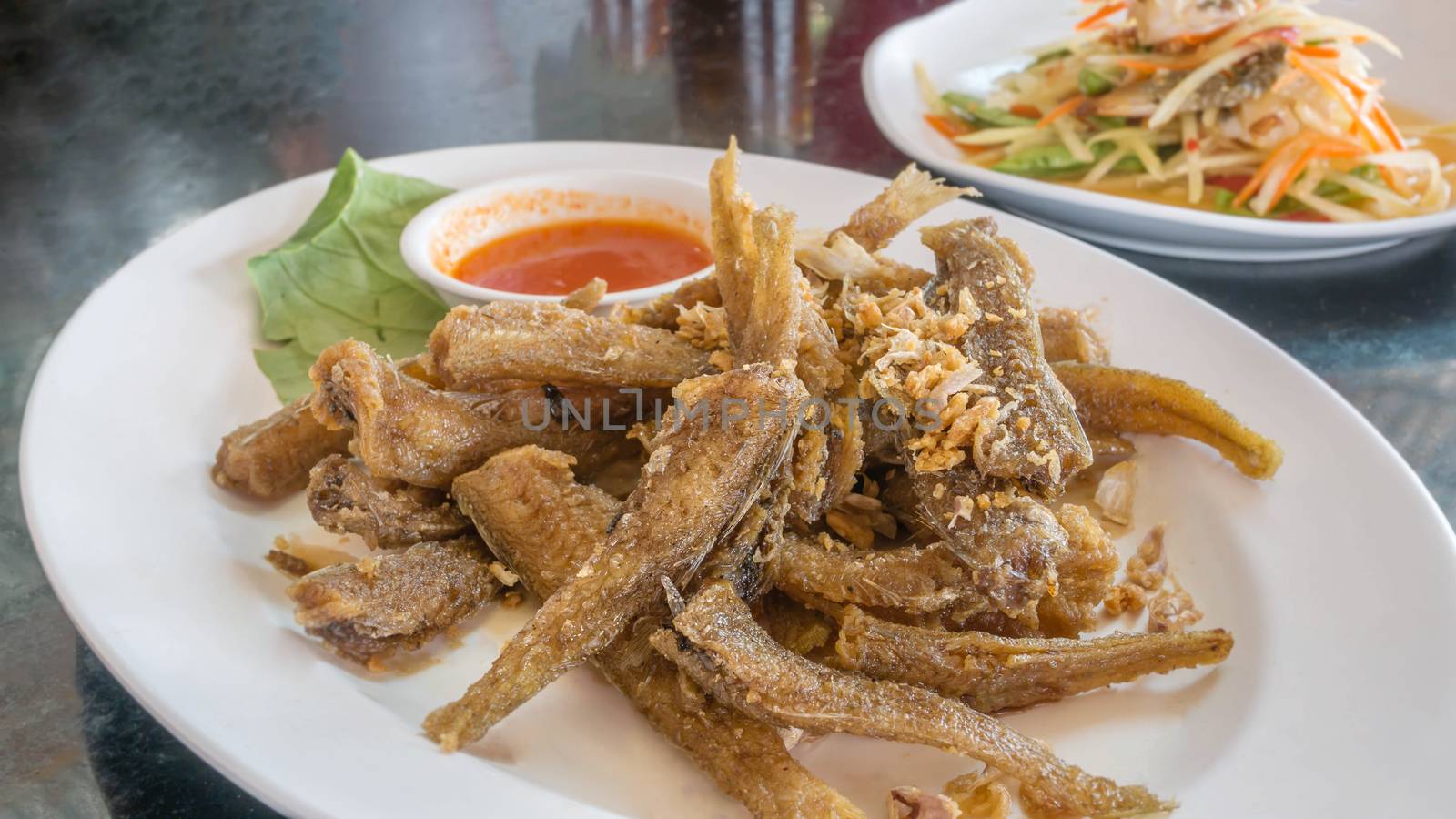 Fried fish topped with garlic served on dish with chili sauce