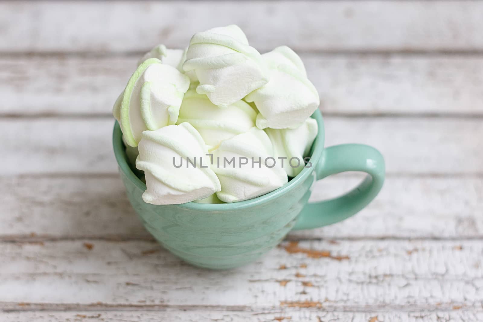 Peppermint large marshmallows in a large green cup on white wooden background