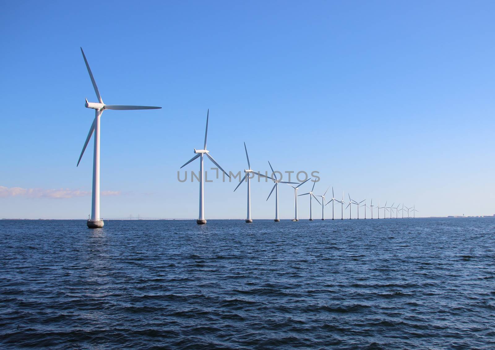 Perspective line of ocean wind mills with dark water and sky
