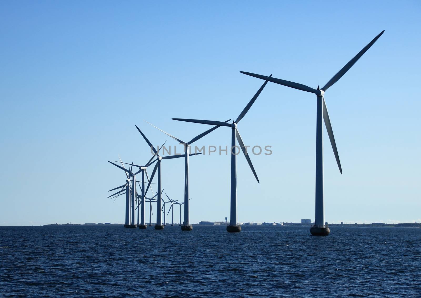 Perspective line of ocean windmills with dark water in back light