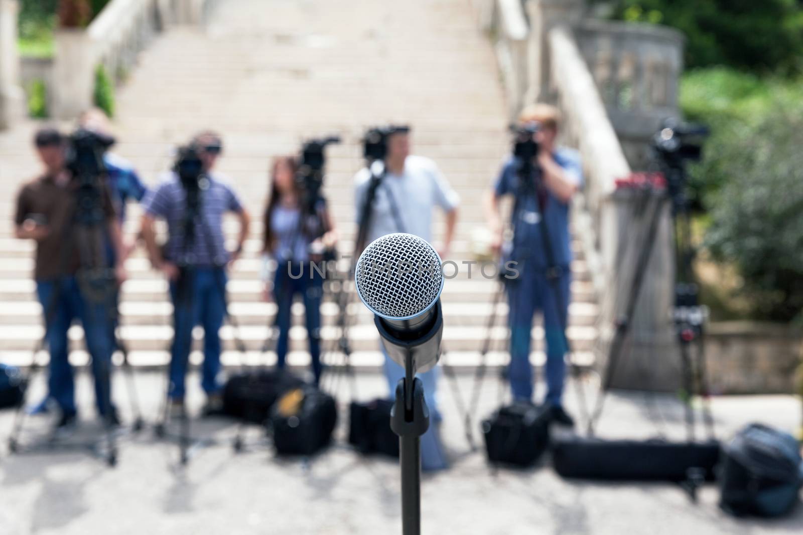 Microphone in focus against blurred camera operators and reporters. Journalism.