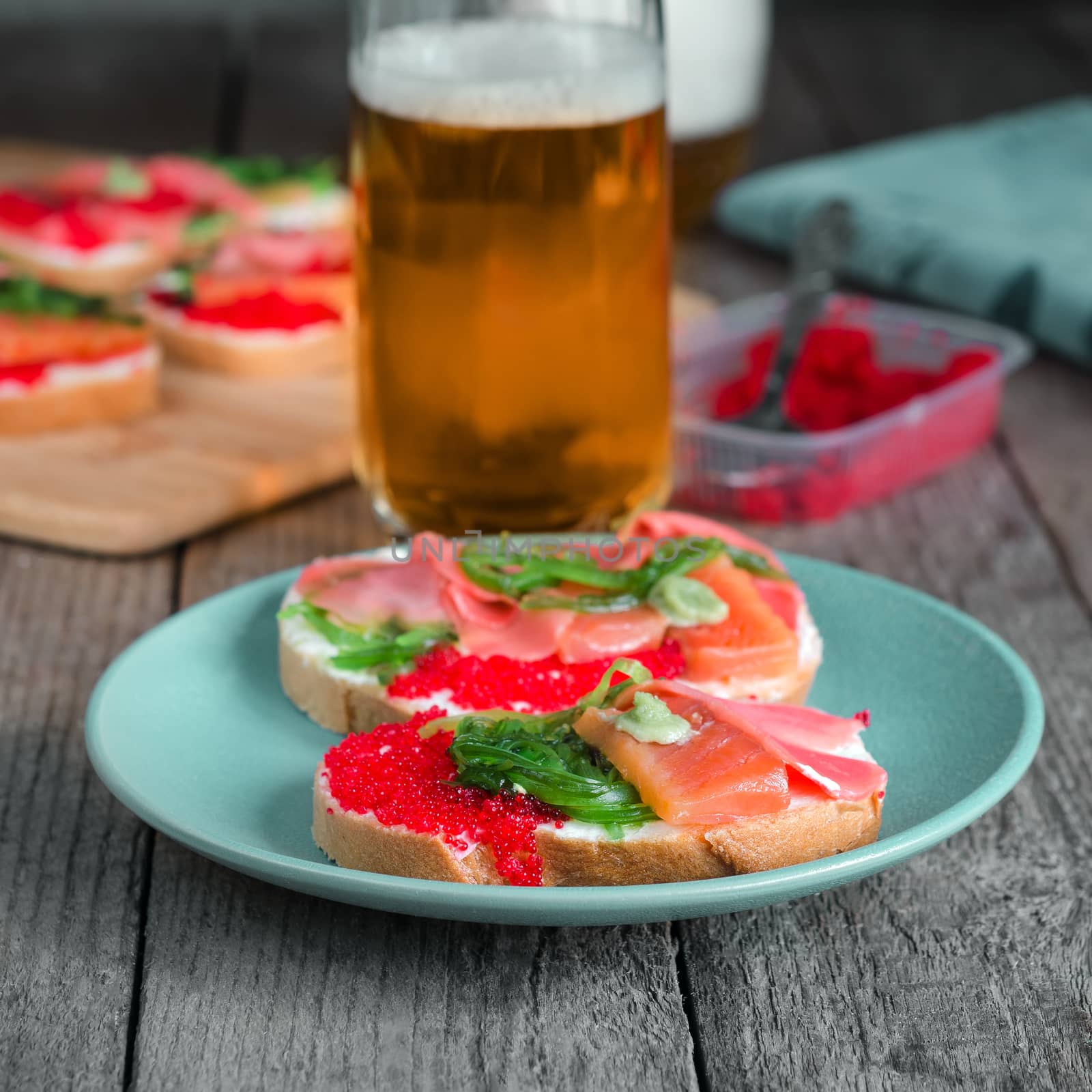 Sandwiches with seafood and beer in the background. Grey background, standing on old wooden surface.