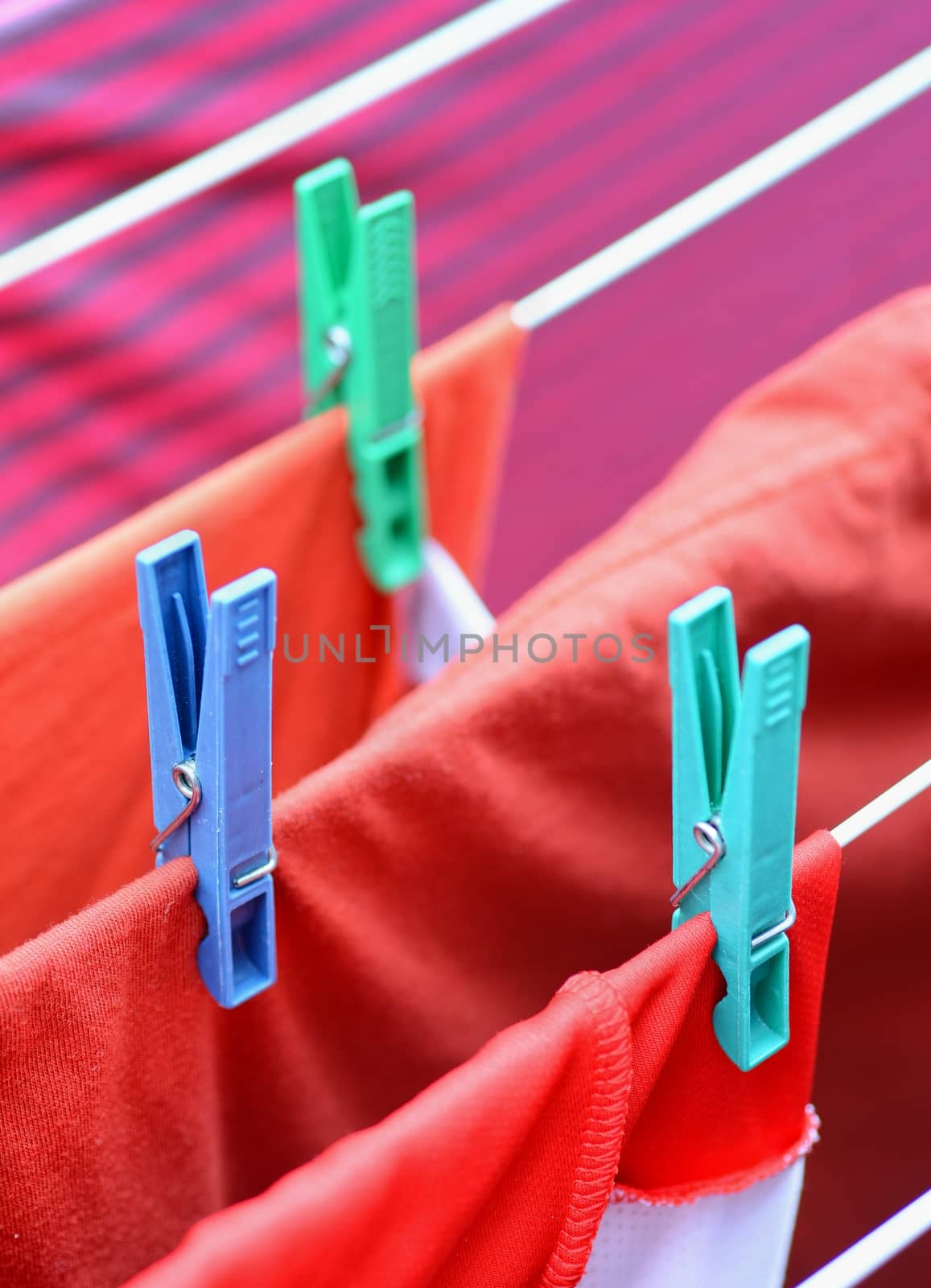 Clothespins on clothesline securing the red wet clothes. Red wet clothes drying on clothesline securing with clothespins.