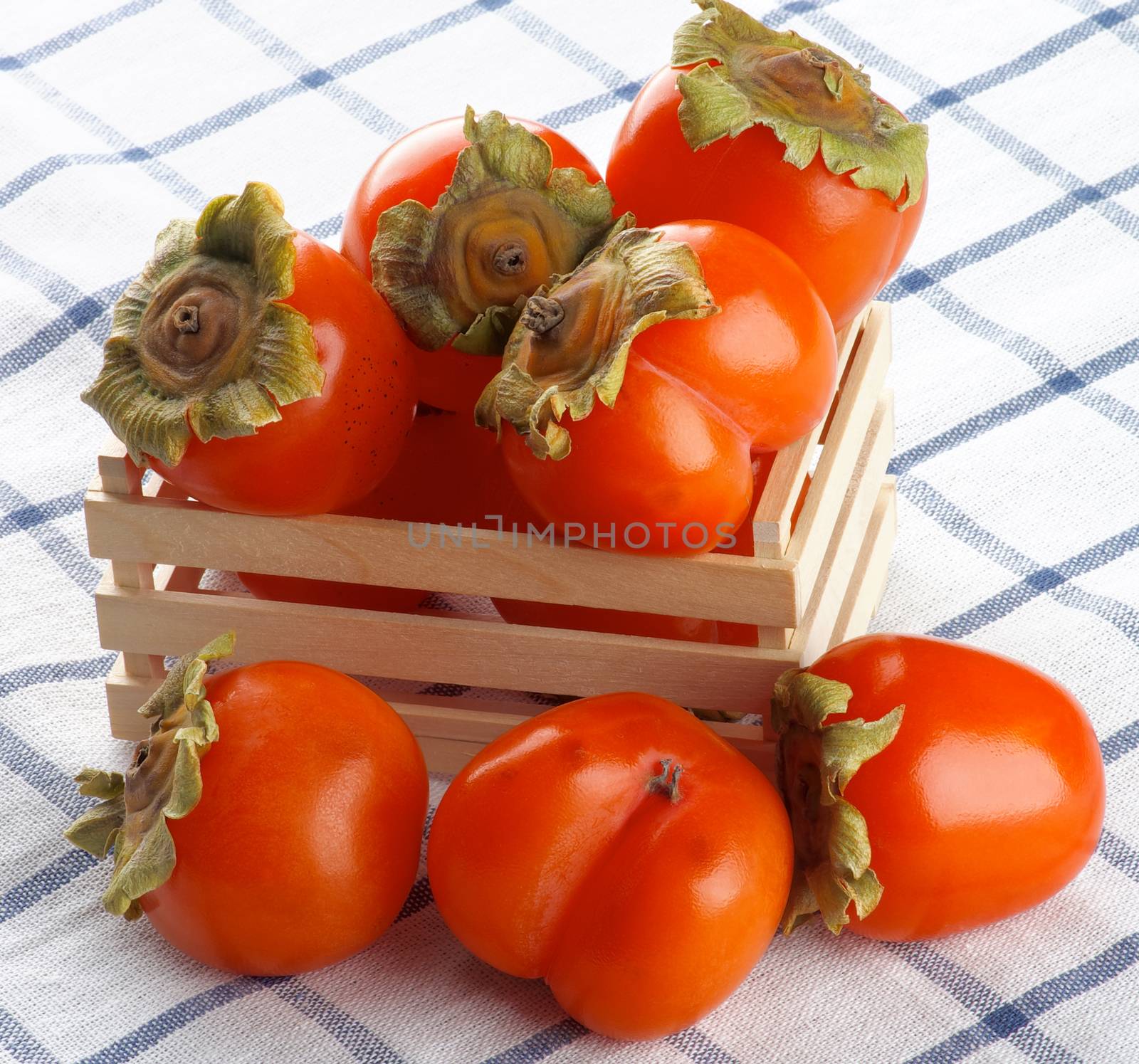 Heap of Delicious Raw Persimmon in Wooden Box closeup on Checkered Textile Napkin
