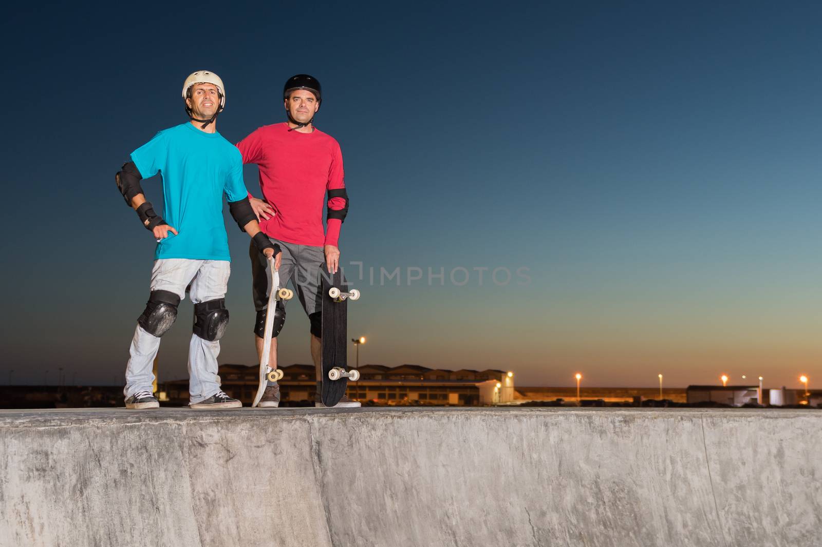 Two skateboarders standing near a concrete pool at skatepark on a beatiful sunset.