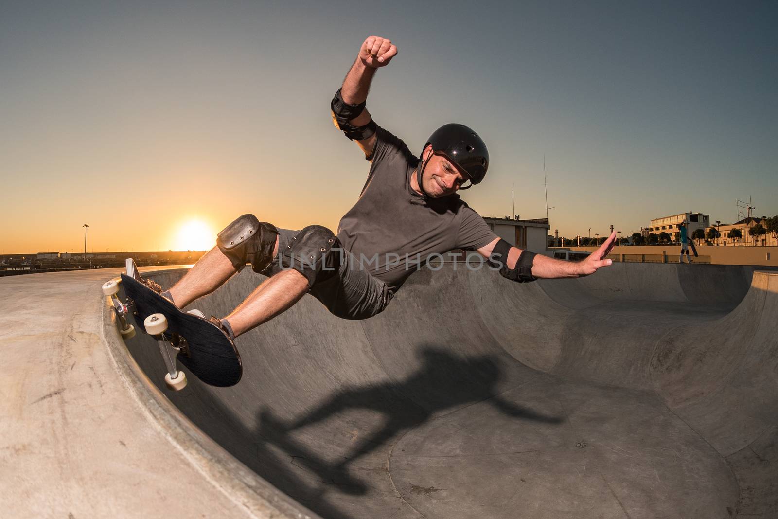 Skateboarder in a concrete pool at skatepark on a beatiful sunset.