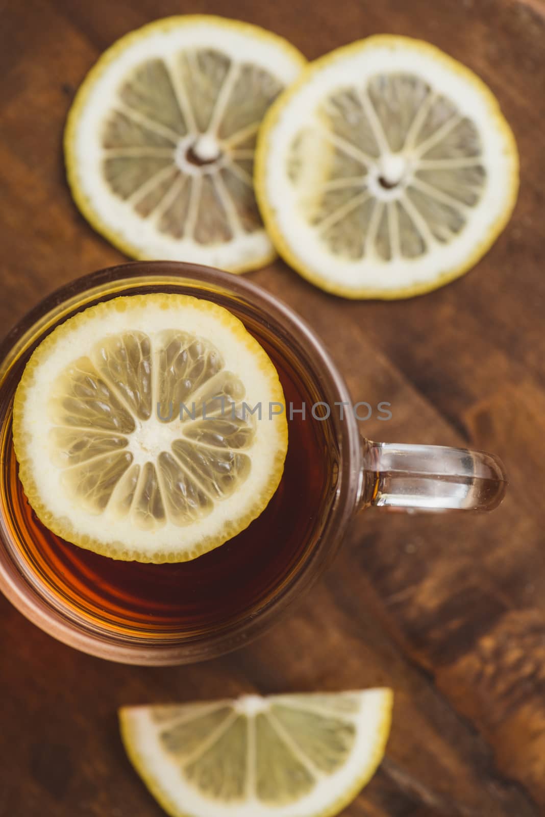 Top view of black tea with lemon in cup and on wooden plank table.