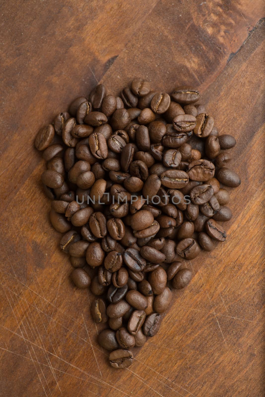 Brown coffee beans in shape of drop, closeup of macro coffee beans for background and texture. On brown wooden board