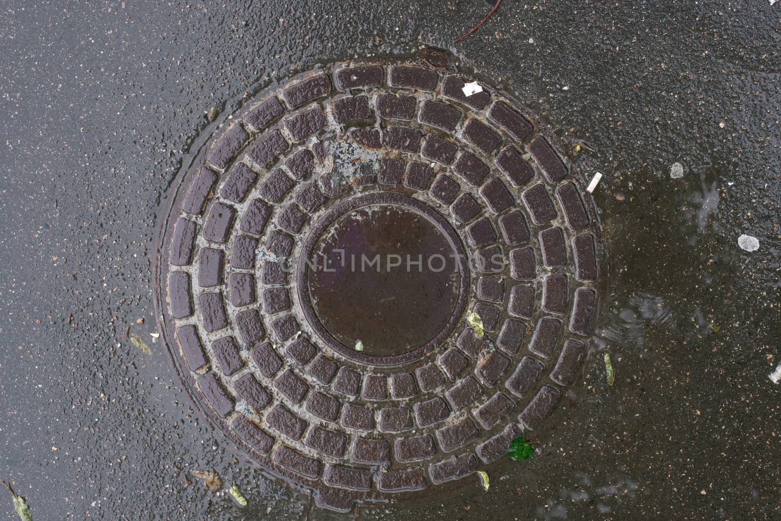 Closeup photo of Old Sewer rust manhole cover on the urban asphalt road. Rain scene