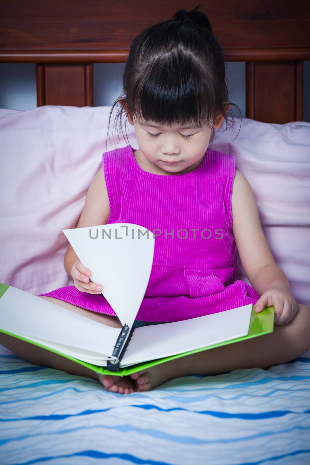 A little cute asian girl in a purple dress sleeping when she read a book on bed in bedroom. Children read and study, sleepy, tired student, education concept.