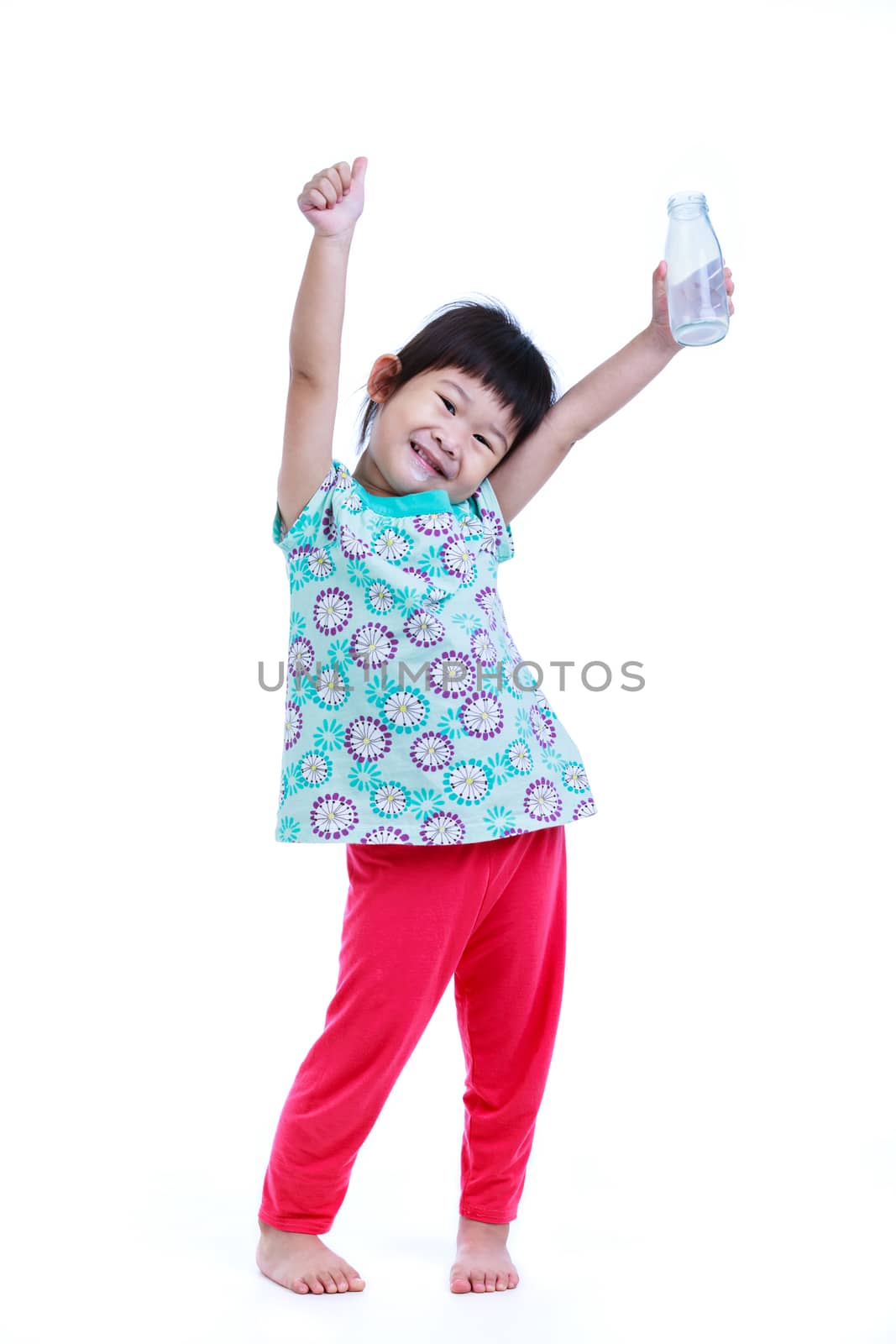 Full body. Fun portrait of pretty asian girl smiling and showing bottle of milk. Drinking milk for good health. Child looking at camera with thumb up, on white background. Studio shoot.