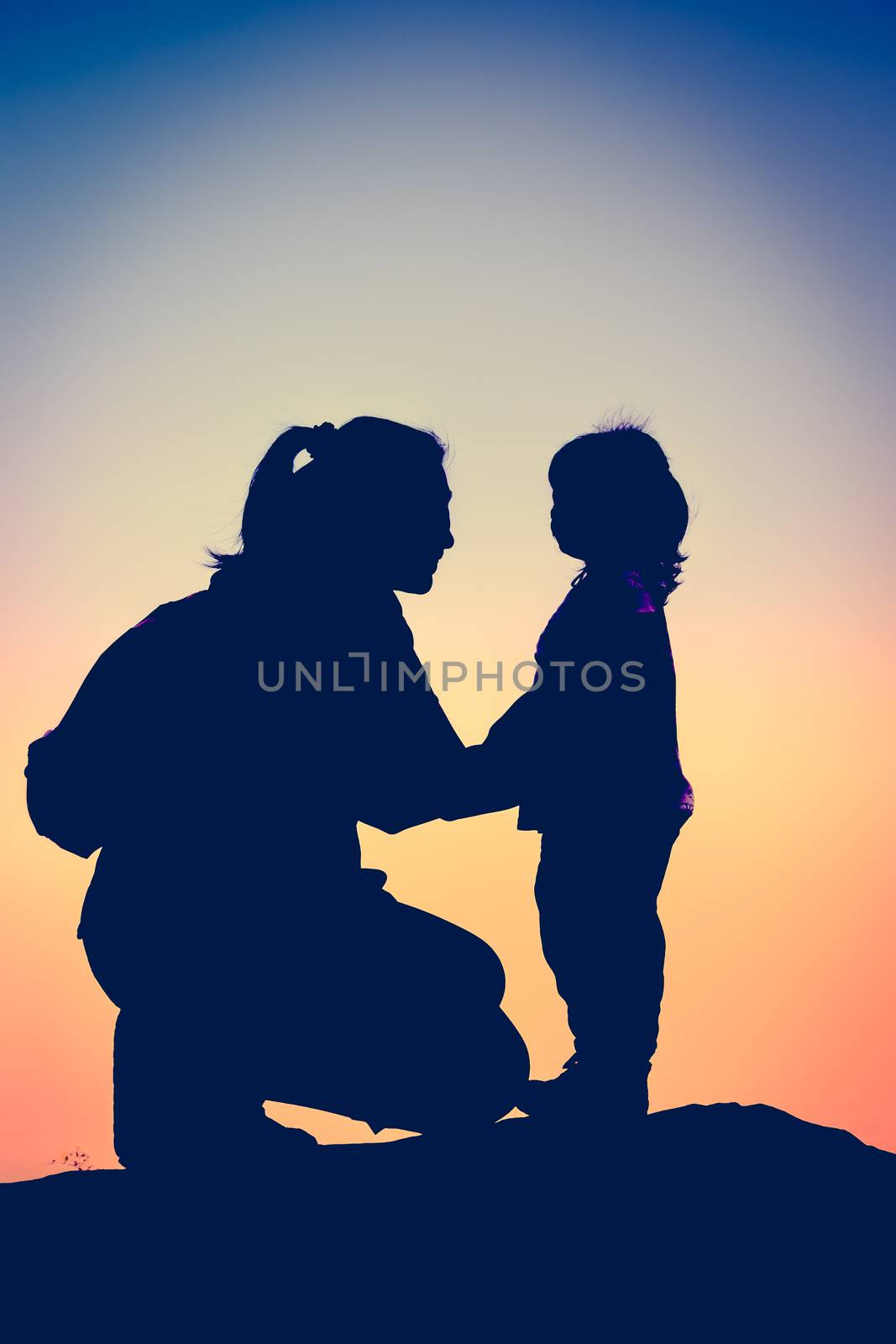 Silhouette side view of young mother and child hikers enjoying the view at the top of a mountain. Colorful sunset sky background. Friendly family. Cross process. Vintage picture style.
