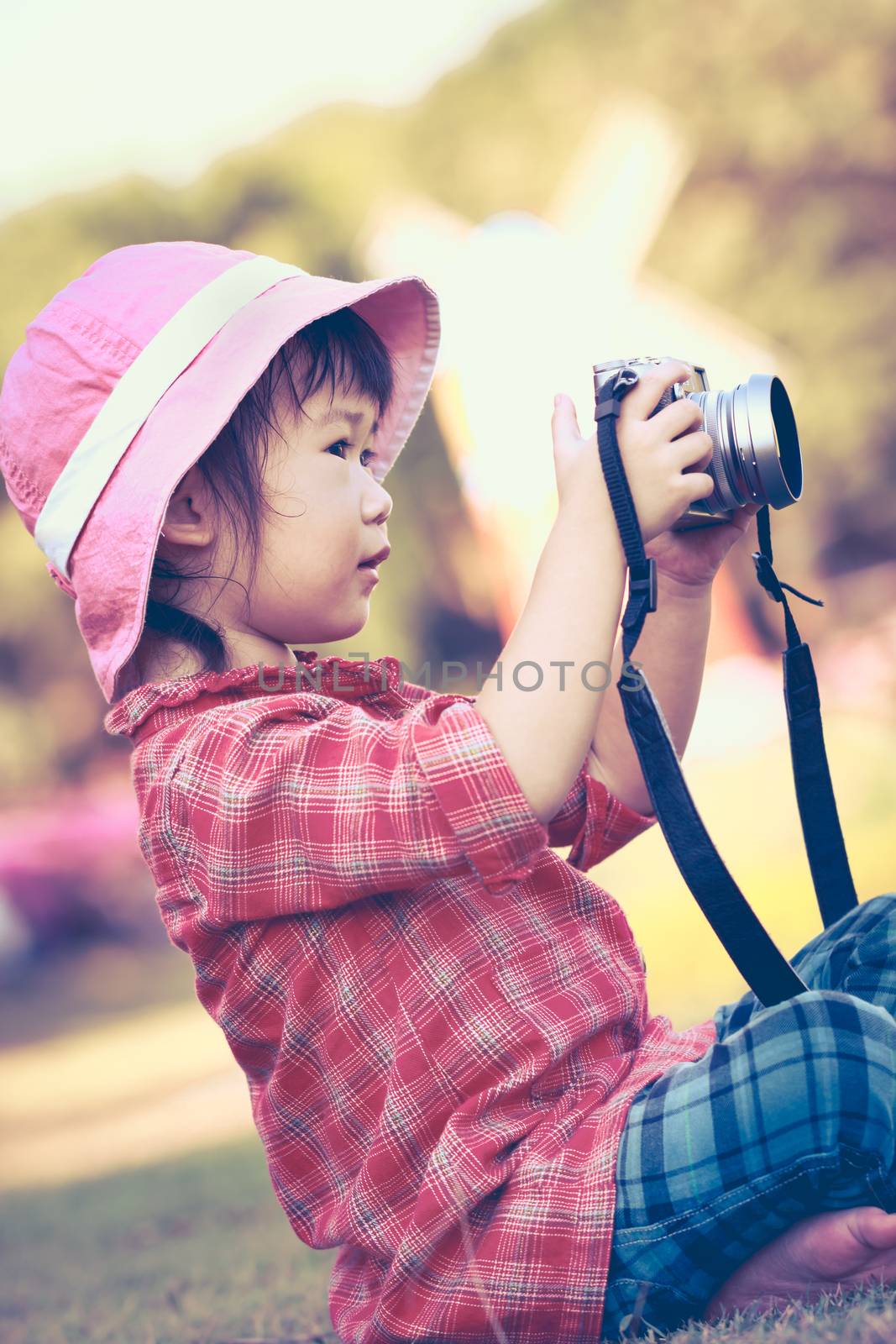 Cute little asian girl taking photos using vintage film camera in the park on blurred background, summer in the day time. Adorable child in nature, outdoors. Vintage style.