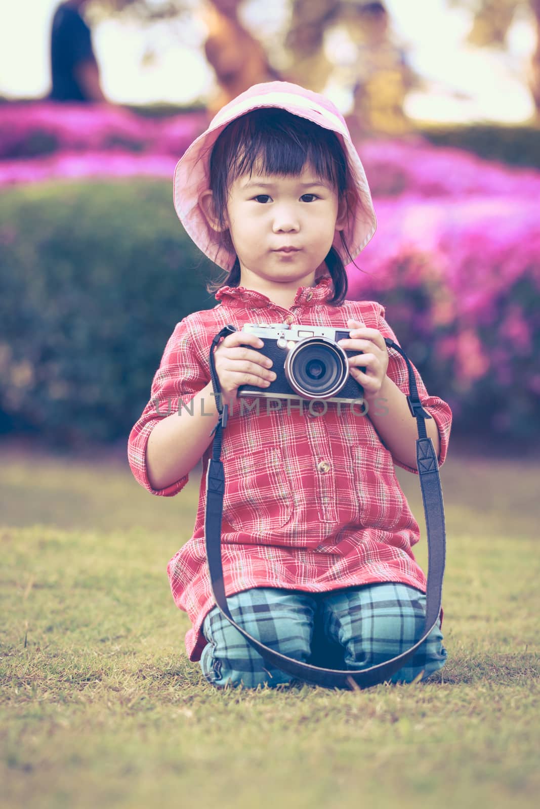 Cute little asian girl holding vintage film camera in the park on blurred background, summer in the day time. Adorable child in nature, outdoors. Vintage style.