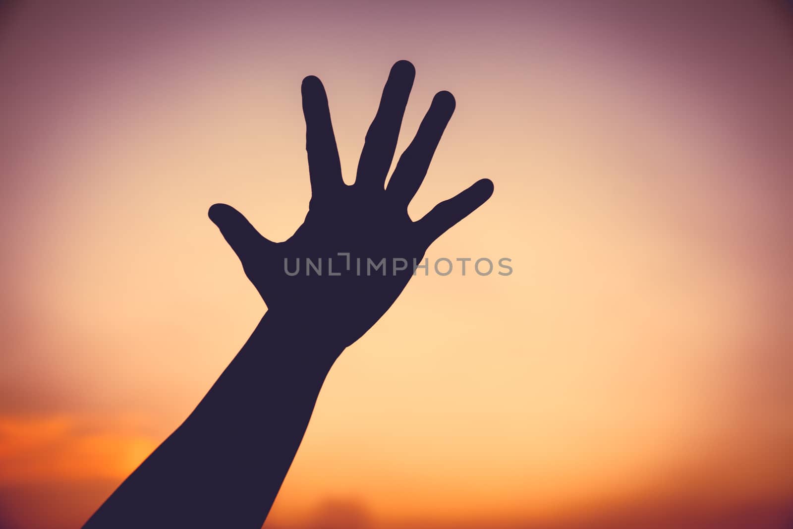Silhouette of a hand on colorful sunset sky background. Symbol is mean to say hi , five , hand up, stop. Outdoors.
