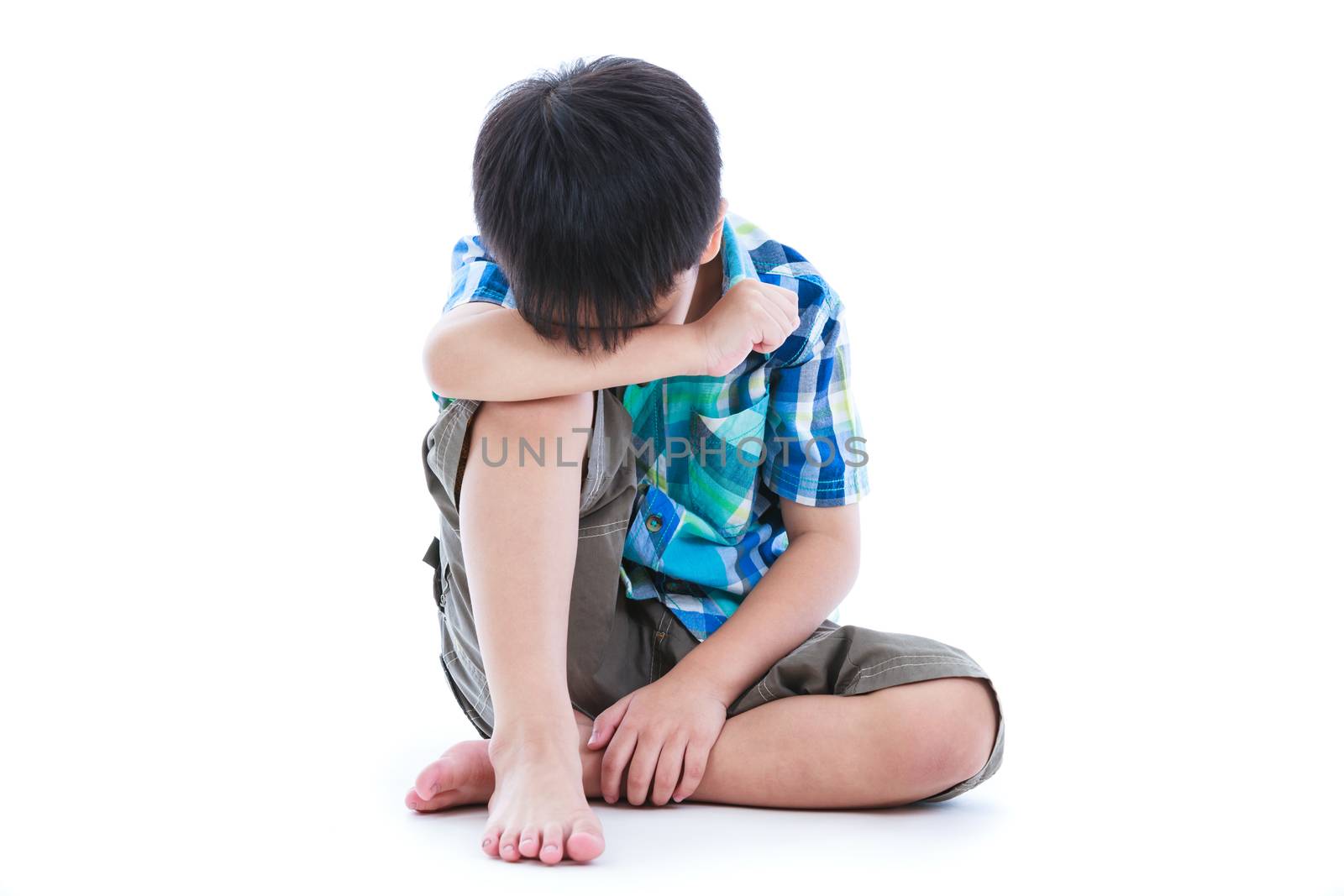 Little sad boy barefeet sitting on floor. Isolated on white background. Negative human emotions. Conceptual about children who lack warmth and affection, abandoned children.