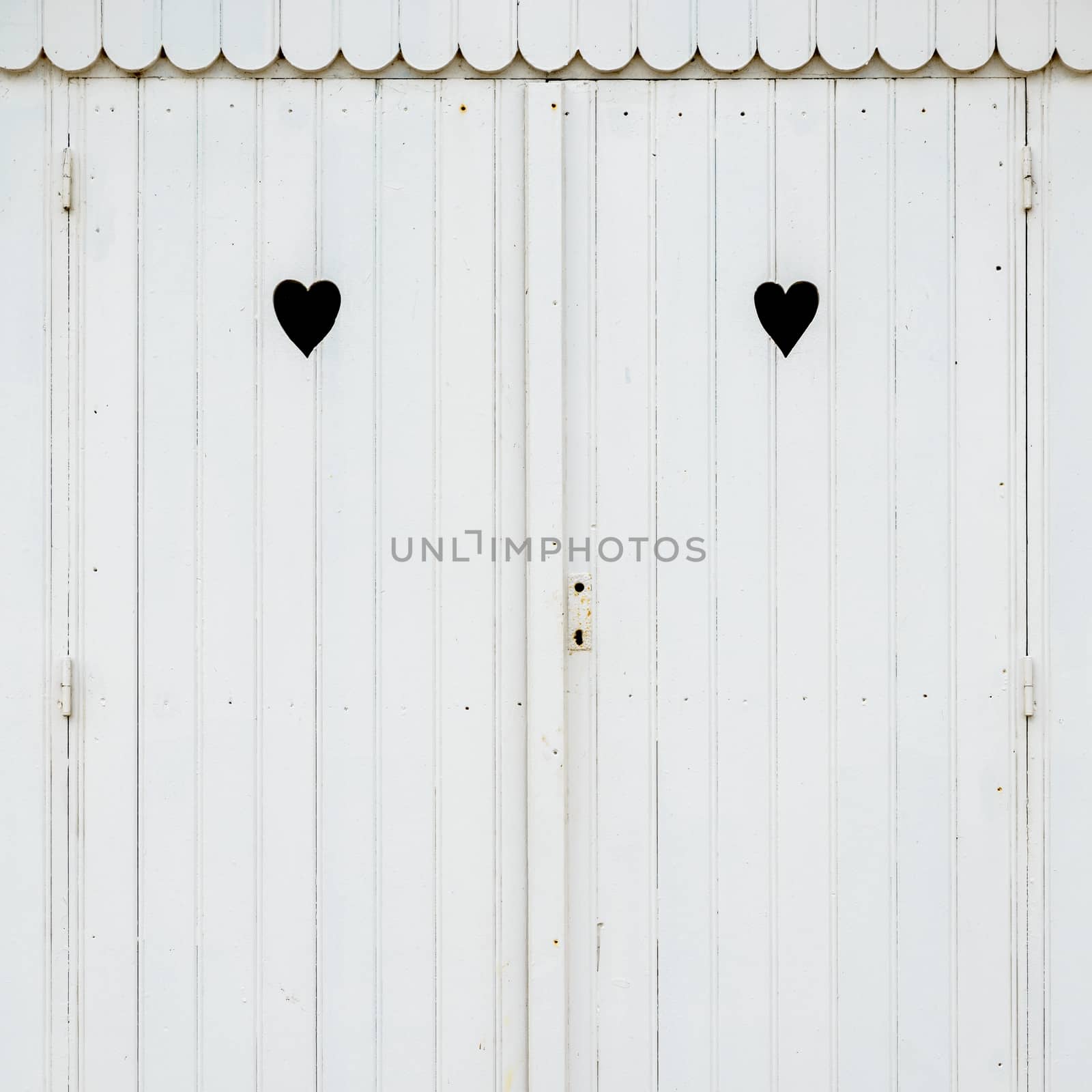 Detail of white wooden beach hut with two carved hearts in the doors.