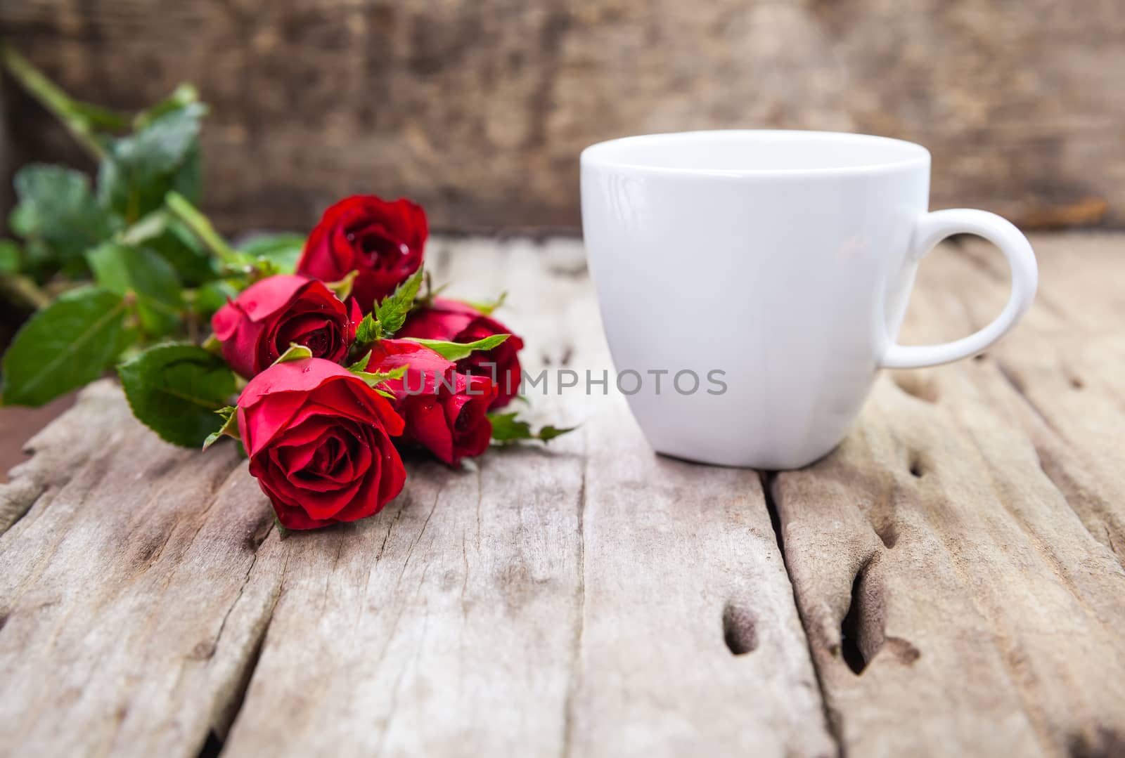 Bouquet of beautiful red roses and coffee cup for Valentine's Day on blurred wooden background. Shallow depth of field (dof), selective focus.