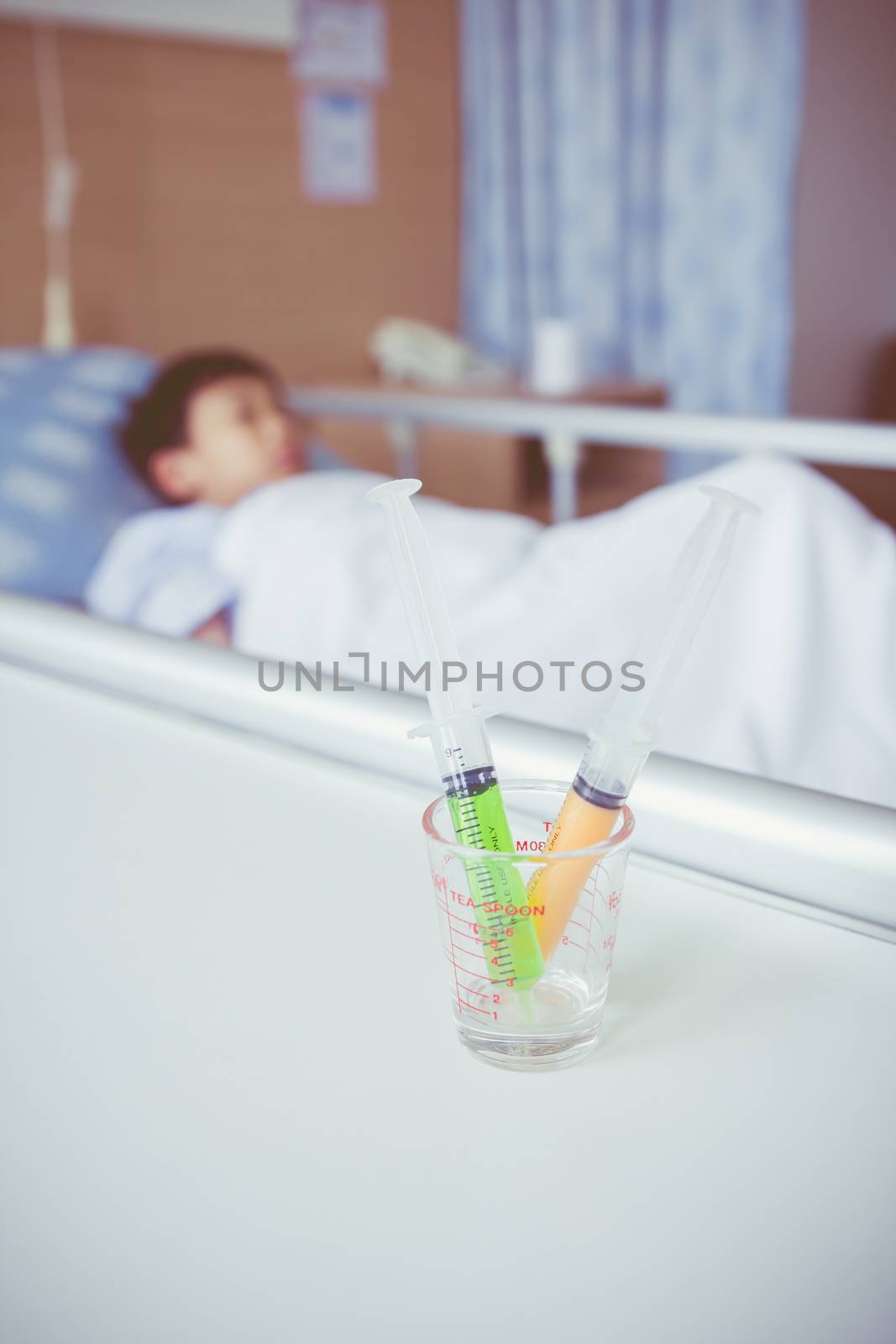 Syringes in a glass measuring cup with blurred illness boy lying by kdshutterman
