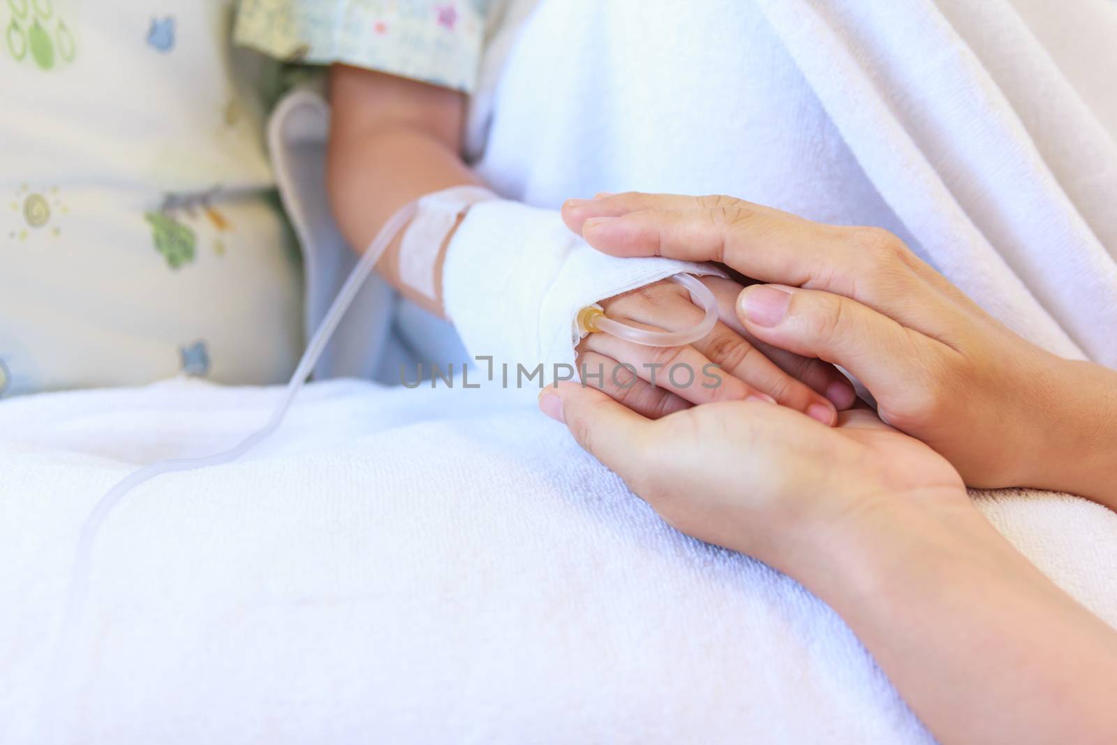 Close up hand of parent holding hand of child in hospital, saline intravenous (IV) on hand, shallow depth of field (DOF) saline intravenous (IV) in focus.