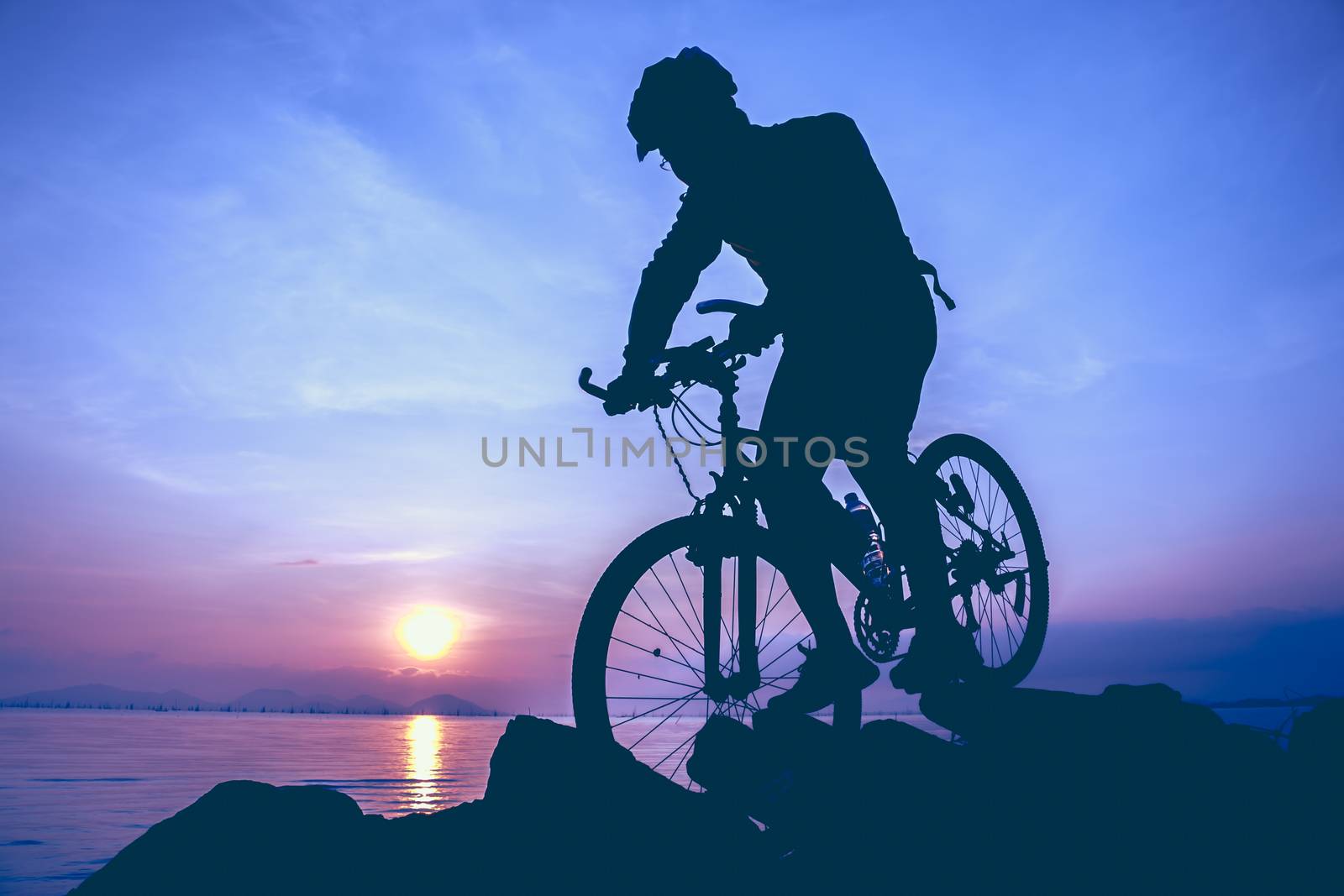Silhouette of bicyclist riding the bike on a rocky trail at seaside, on colorful sunset sky background. Active outdoors lifestyle for healthy concept. Vintage style.