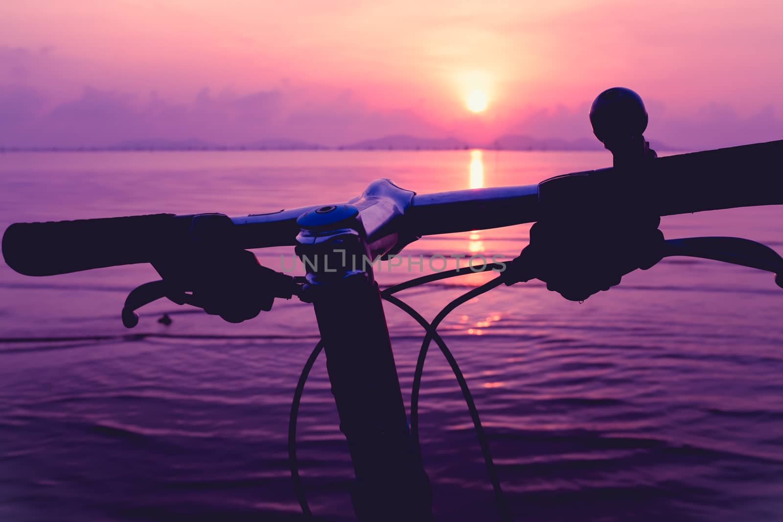 Silhouette of a parts bicycle, handlebar on the beach against colorful sunset in the sea, purple sky background. Reflection of sun in water. Outdoors.