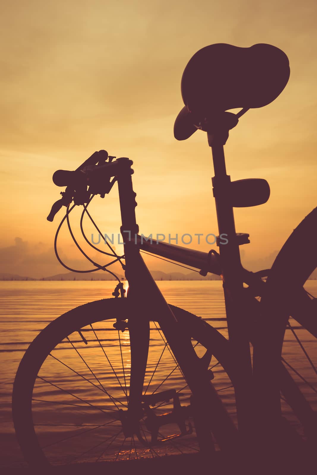 Silhouette of bicycle on the beach against colorful sunset in the sea, orange sky background. Outdoors. Vintage picture style.