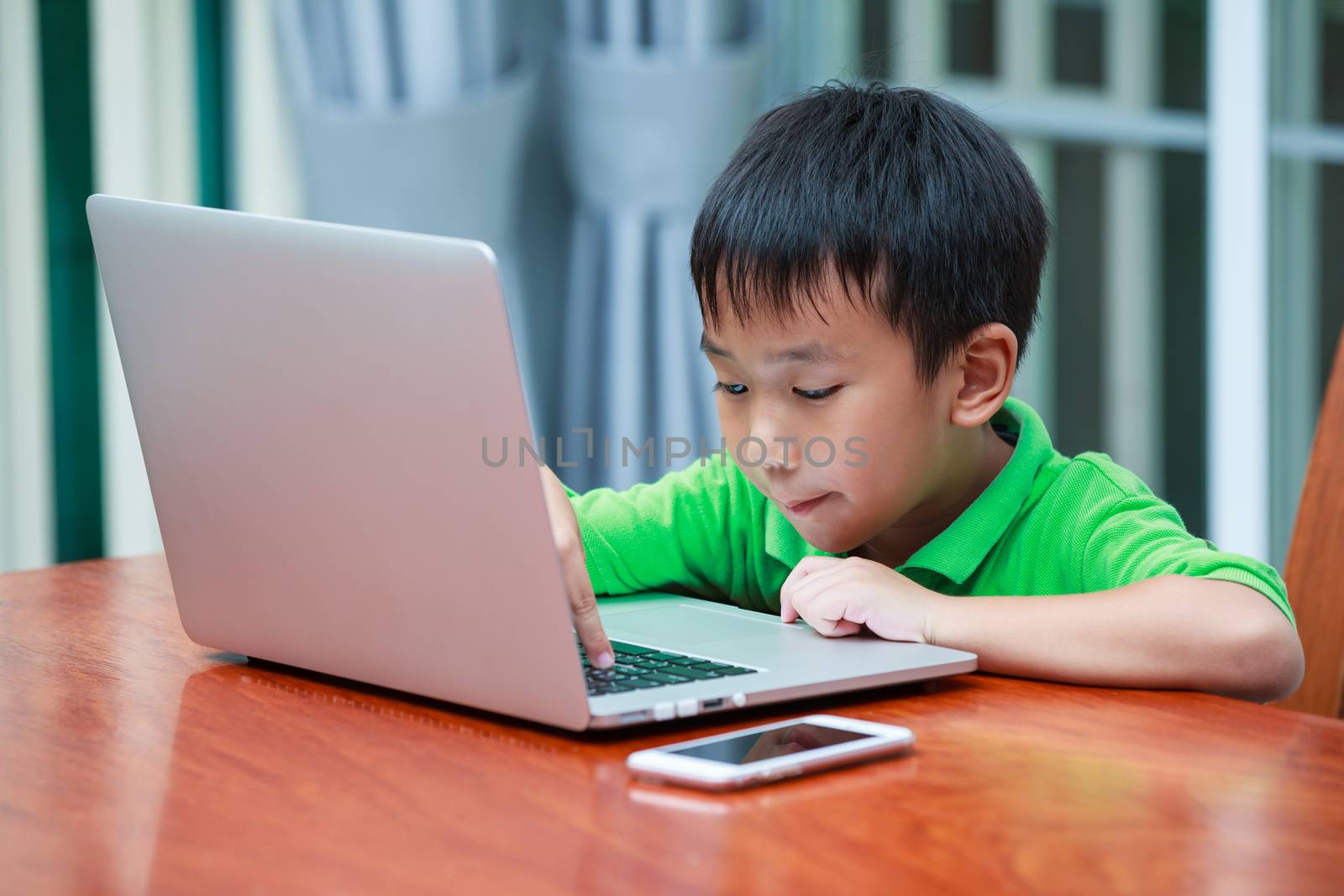 Happy asian child. Handsome boy enjoying modern generation technologies playing indoors using laptop computer and mobile phone. Education and learning concept.