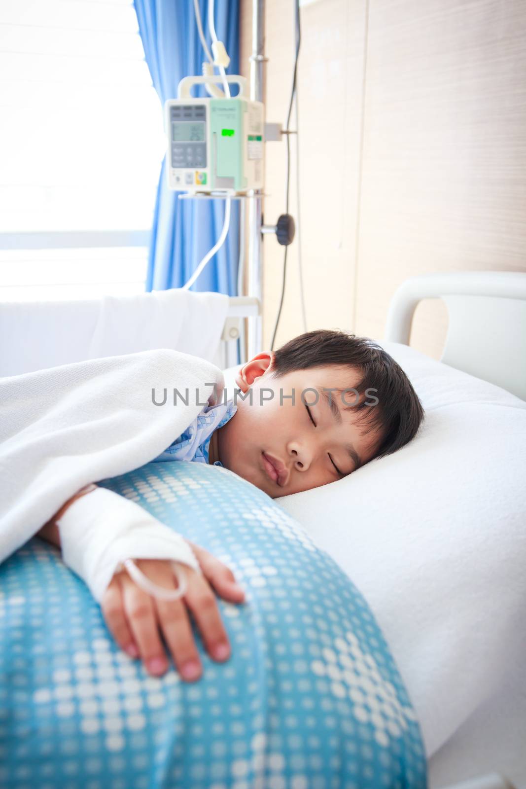 Illness asian boy sleeping at modern and comfortable equipped hospital room with saline intravenous (IV) on hand. Health care and people concept.