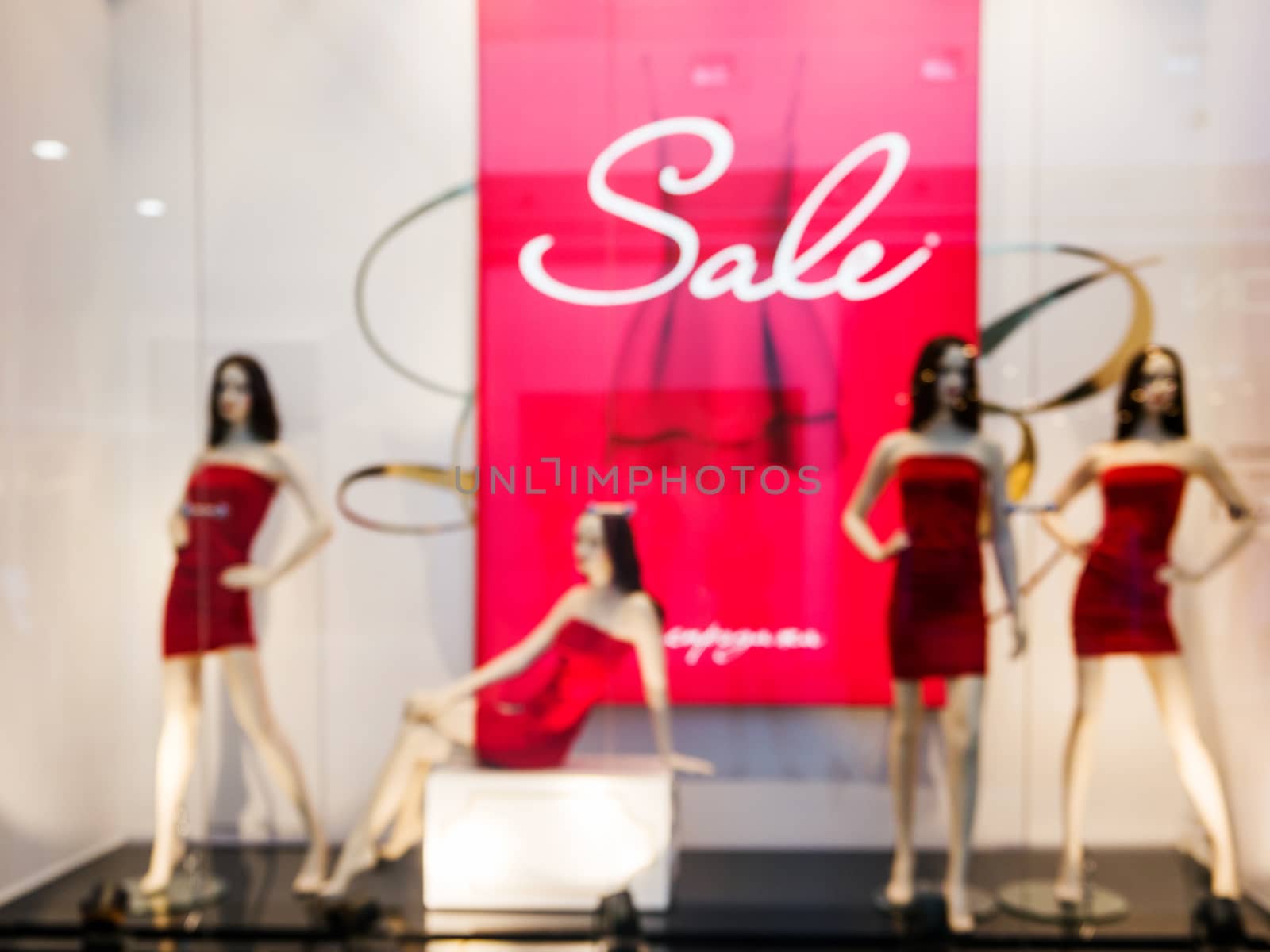 Blur image of window bright display with four mannequins wearing red dress with text Sale