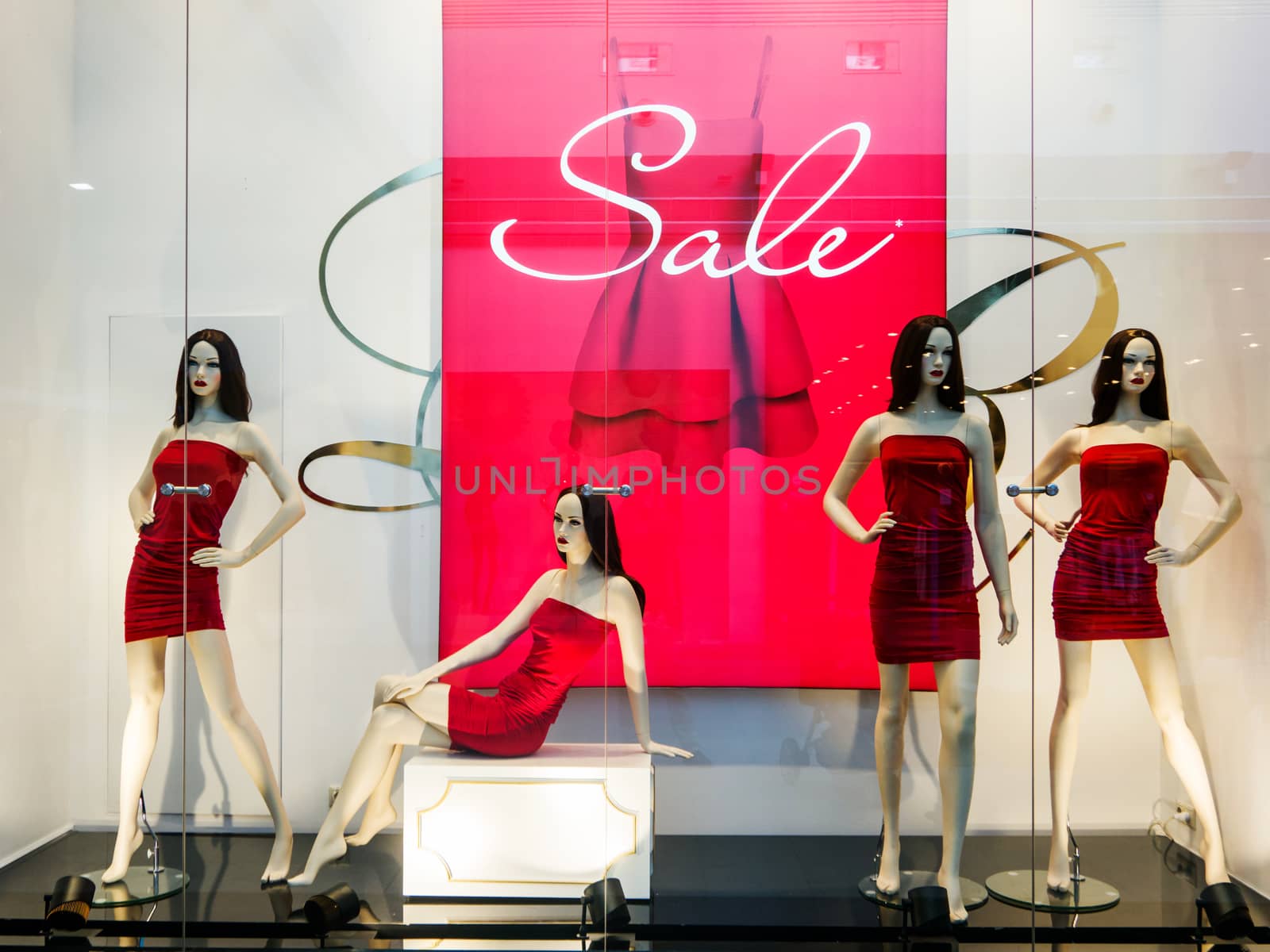 Window bright display with four mannequins wearing red dress with text Sale