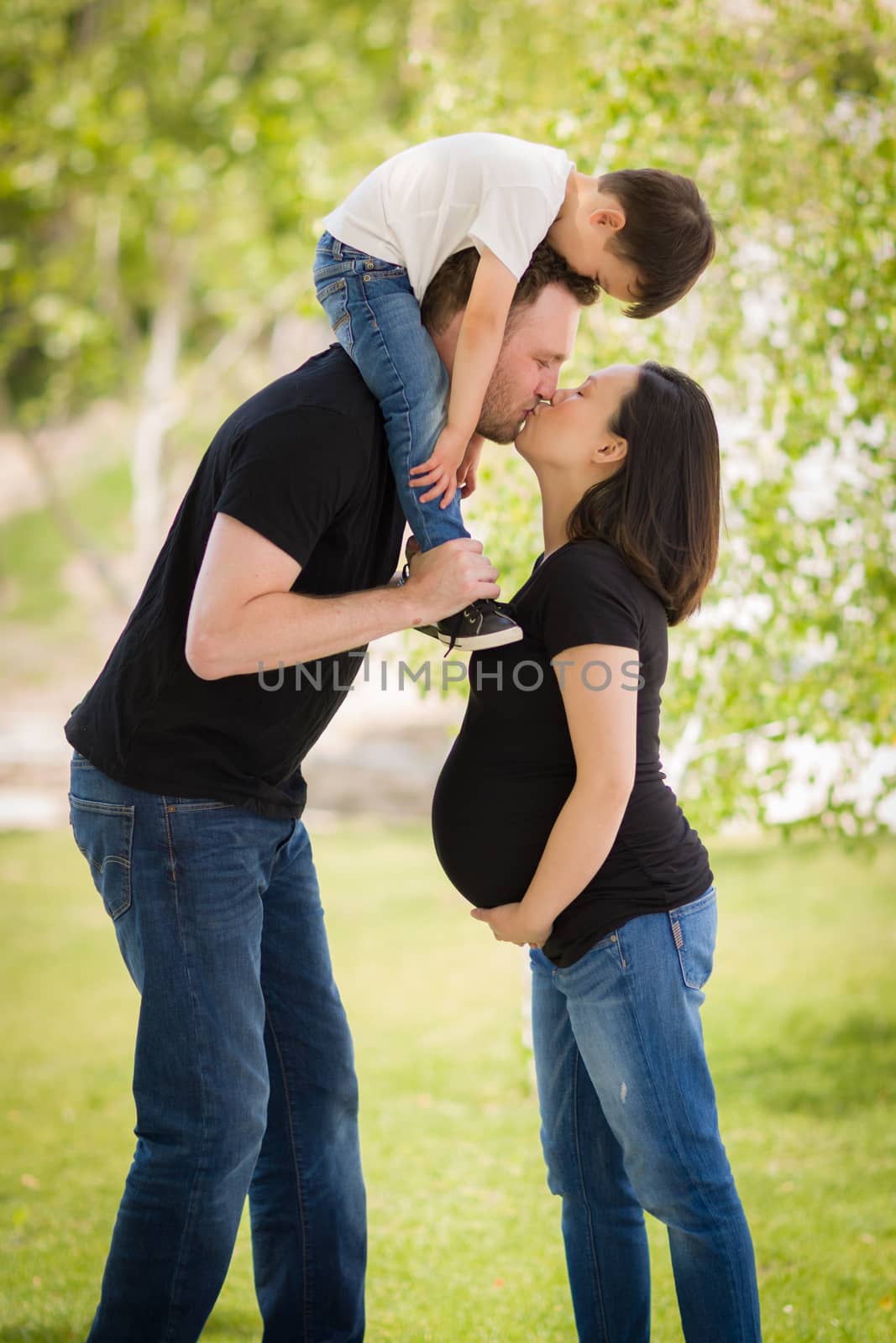 Loving Pregnant Mixed Race Couple Kissing with Young Son Riding Piggyback.