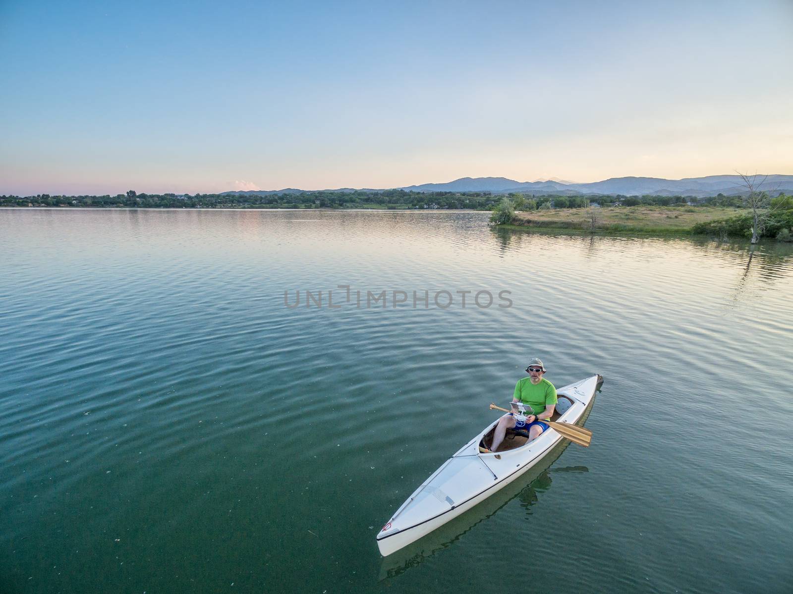 male paddler is operating a drone from a canoe on a lake, aerial view