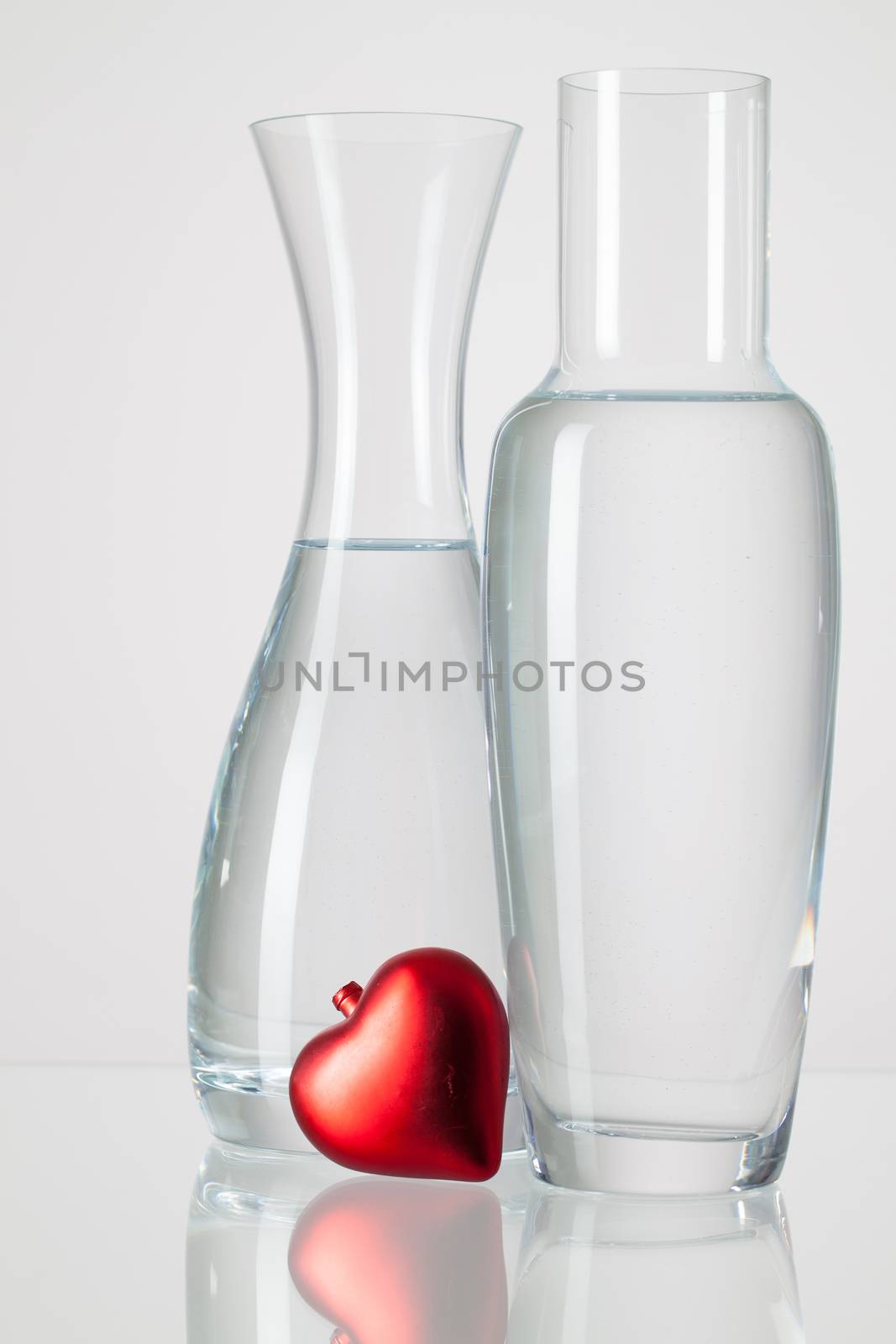 Two vases with clean water and red heart  on a glass table
