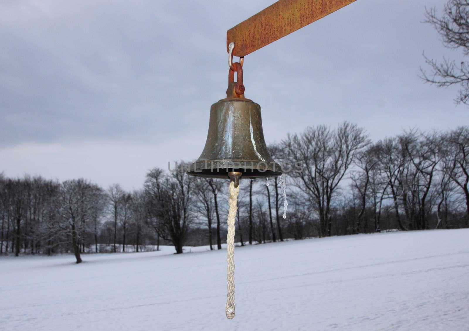 Metal Bell with Winter Snowy Fields in Background. The Bell is used on a golf course.