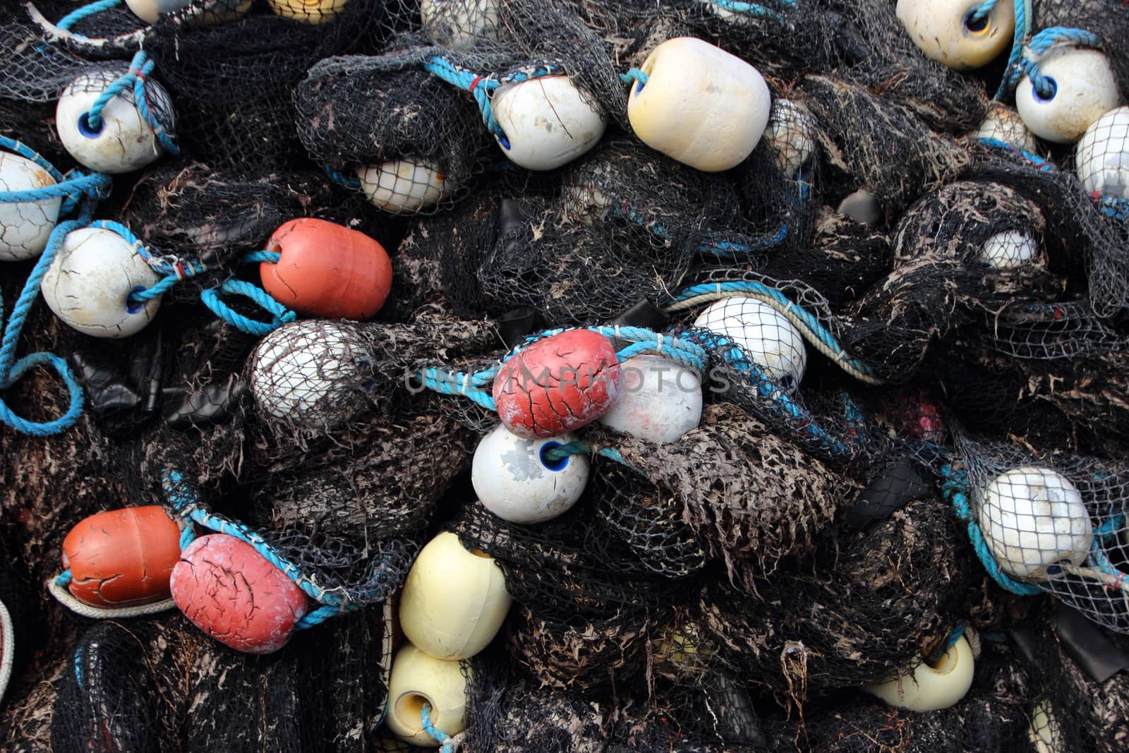 Closeup on Black Fishing Net Pile with Colored Float in Background
