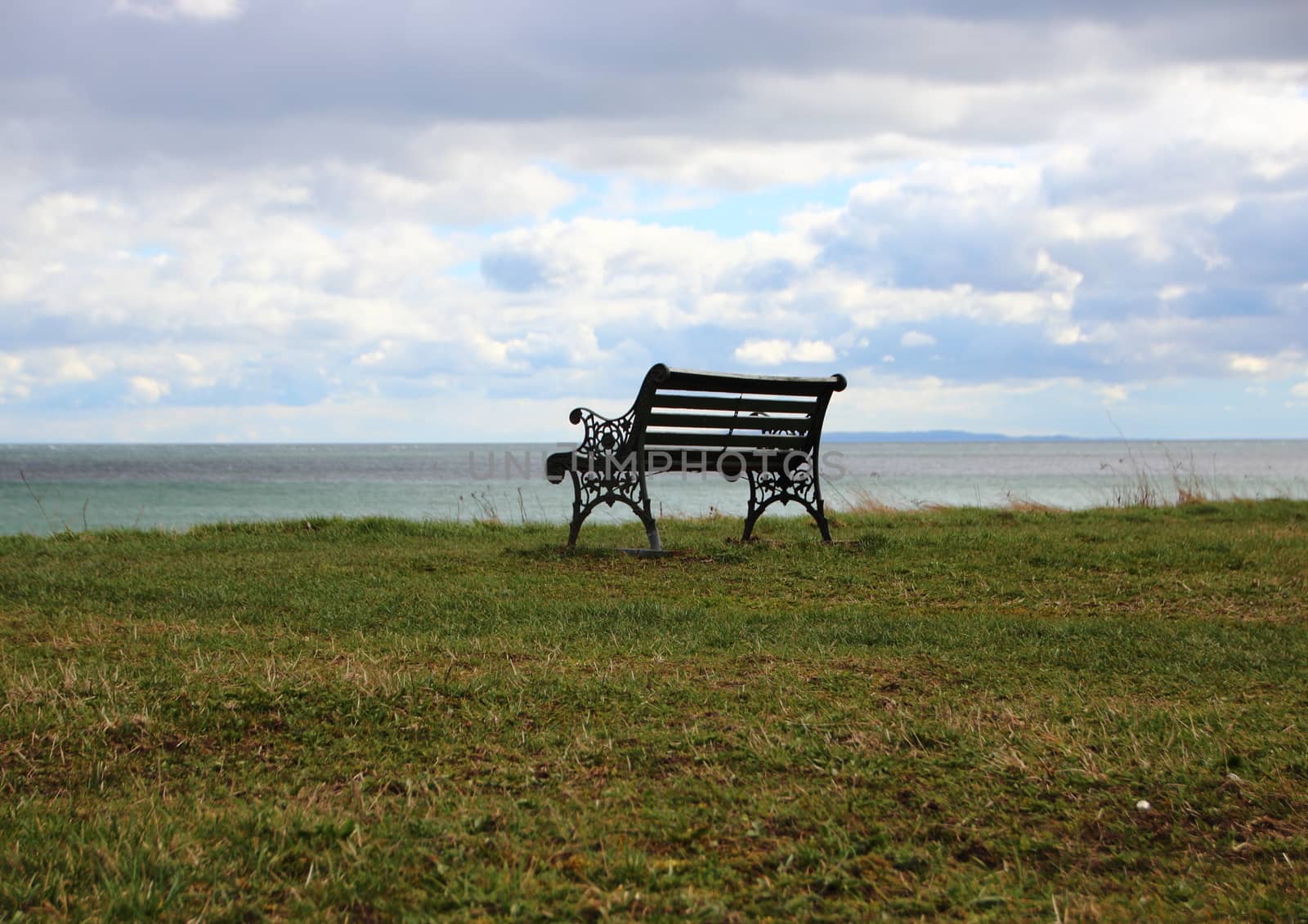 Single Outdoor Iron Bench at Ocean with Clouds by HoleInTheBox